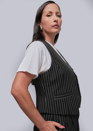 1X=Woman wearing a black pinstripe apron over a white shirt on a light gray background