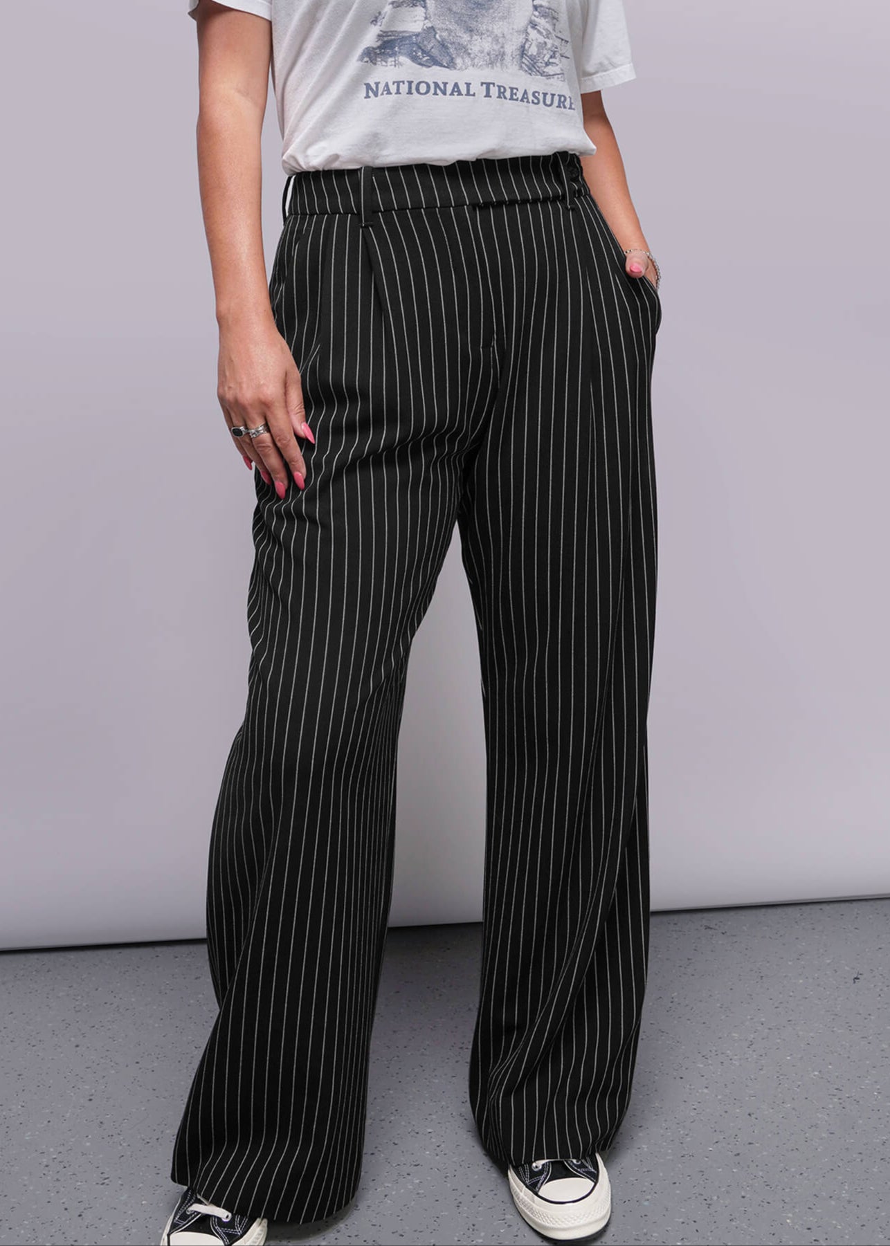 S=Person wearing a graphic t-shirt and pinstripe pants against a plain background