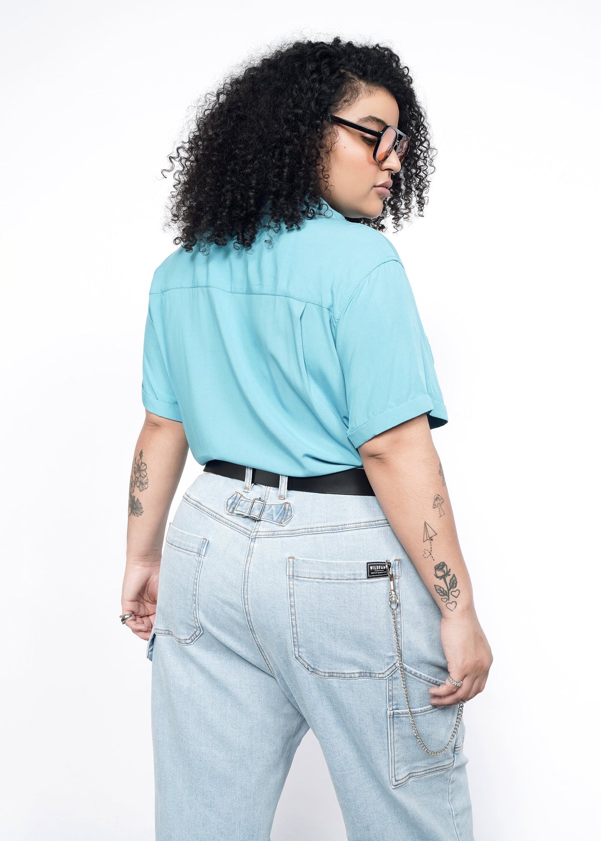 Back image of Model wearing the Empower Button Up in Coastal with Floral print piped trim in size 1X, tied in a knot at waist, with jeans, a black belt, and sunglasses