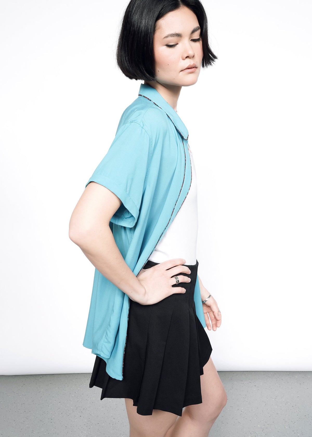 Side image of Model wearing the Empower Button Up in Coastal with Floral print piped trim in size XS, with a white T, black skirt