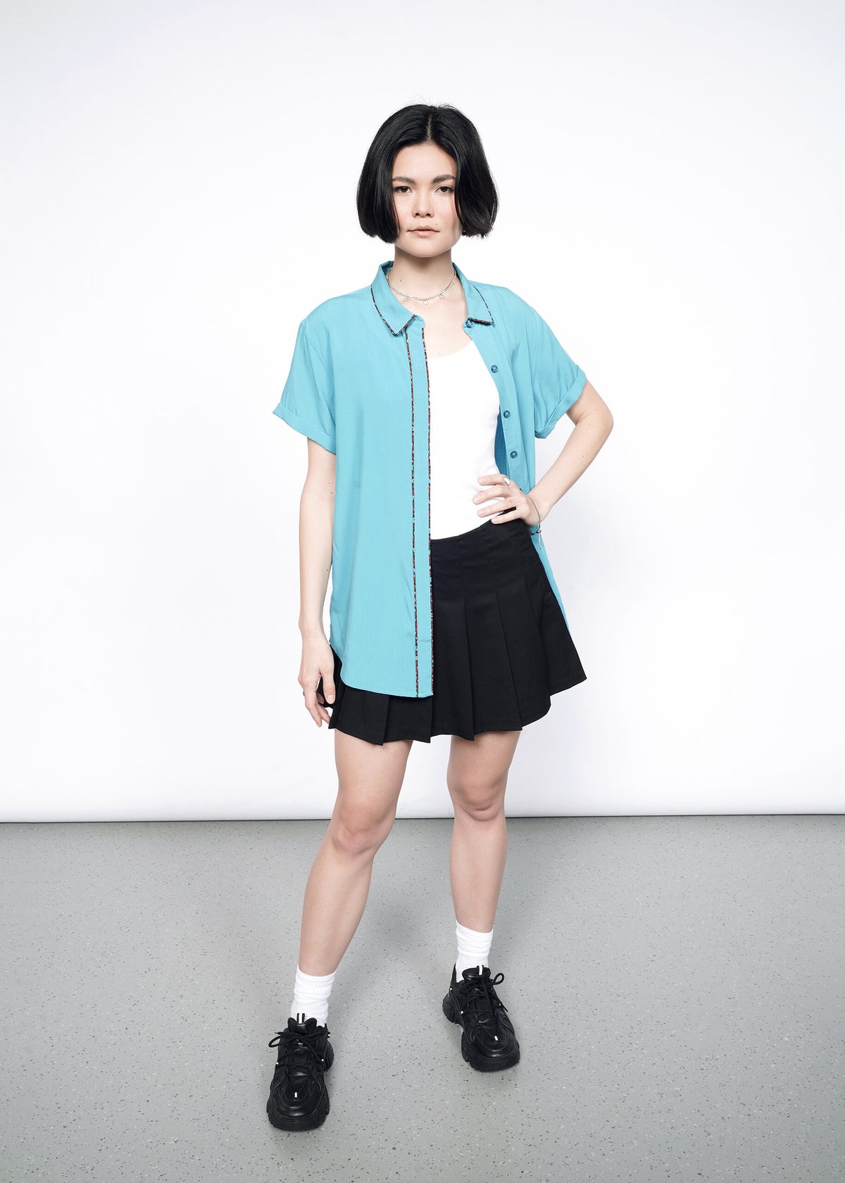 Model wearing the Empower Button Up in Coastal with Floral print piped trim in size XS, with a white T, black skirt, white socks, and black shoes. 