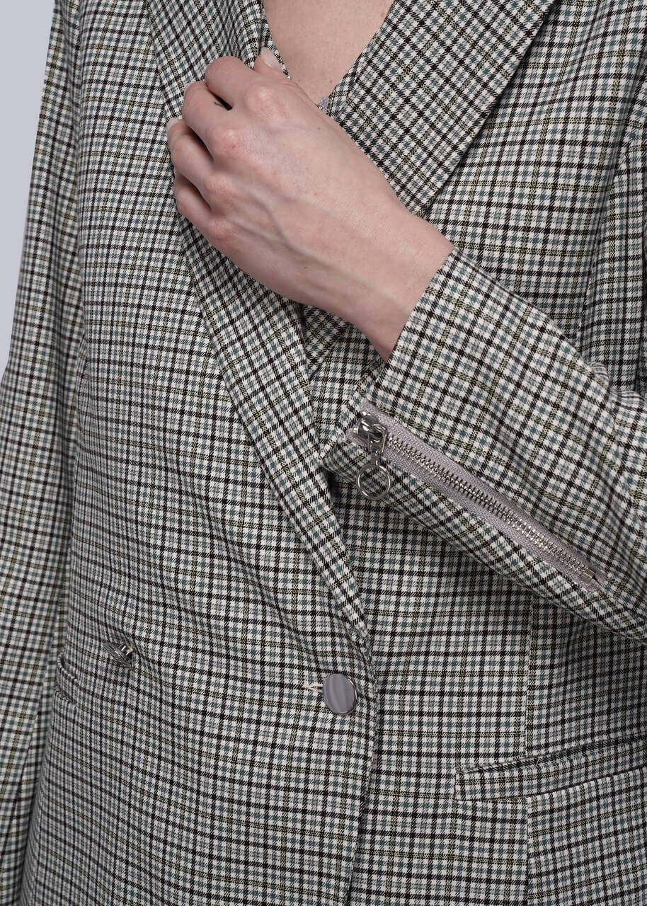 S=Close-up of a person wearing a checkered blazer with a hand adjusting the collar.
