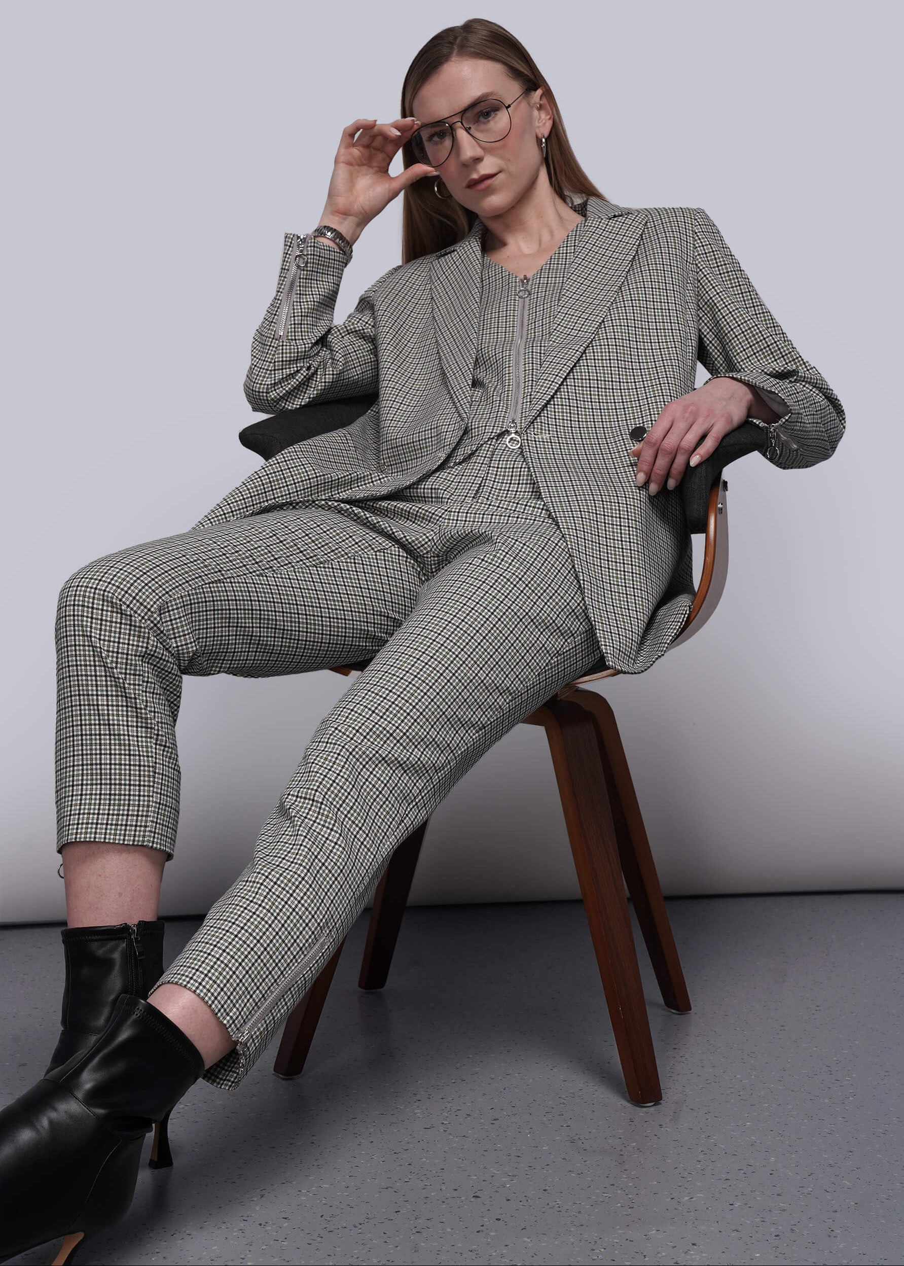 S=Person in a gray checkered suit sitting on a chair against a plain background