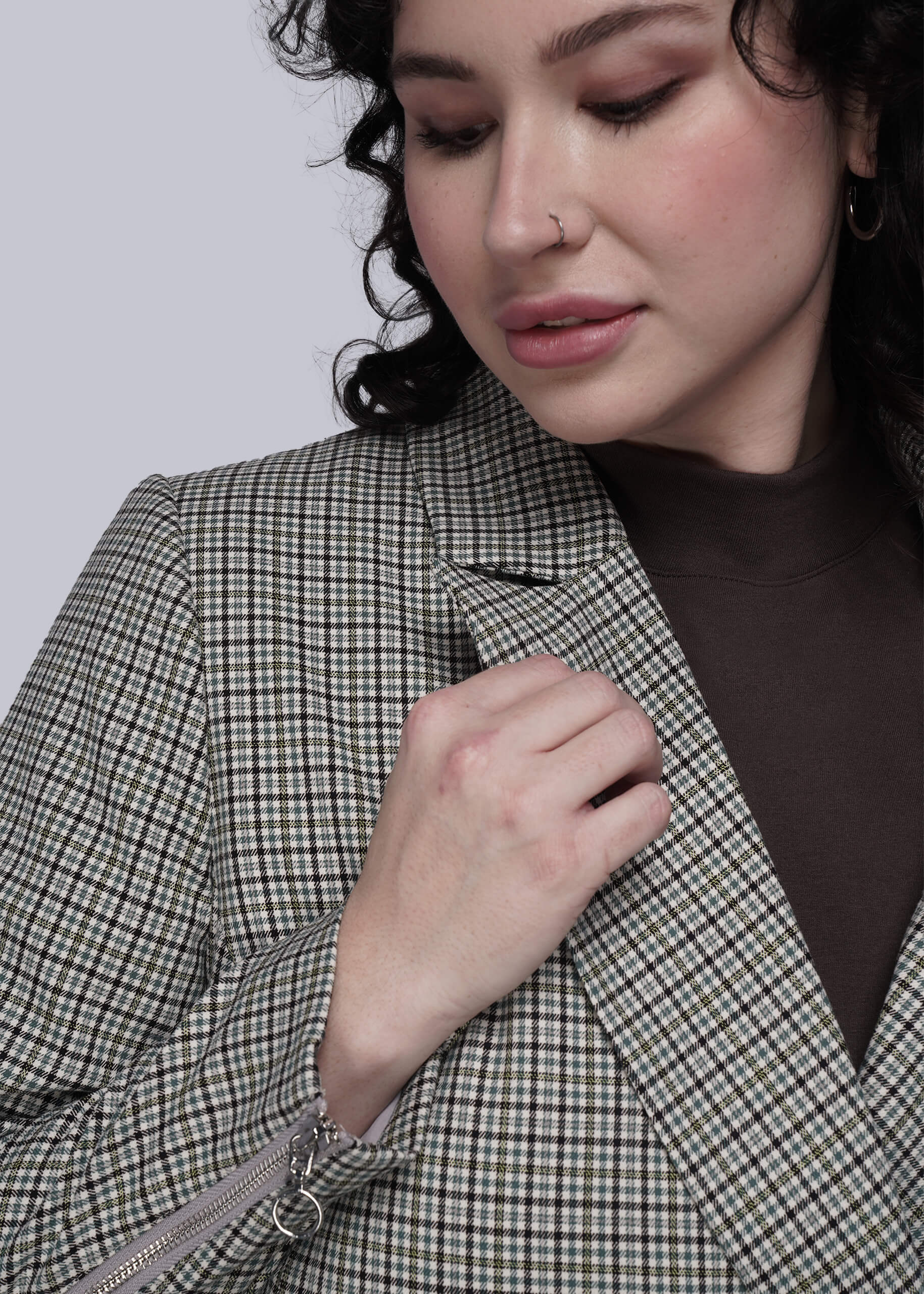 S=Close up of person wearing a checkered blazer with hand on collar against a plain background