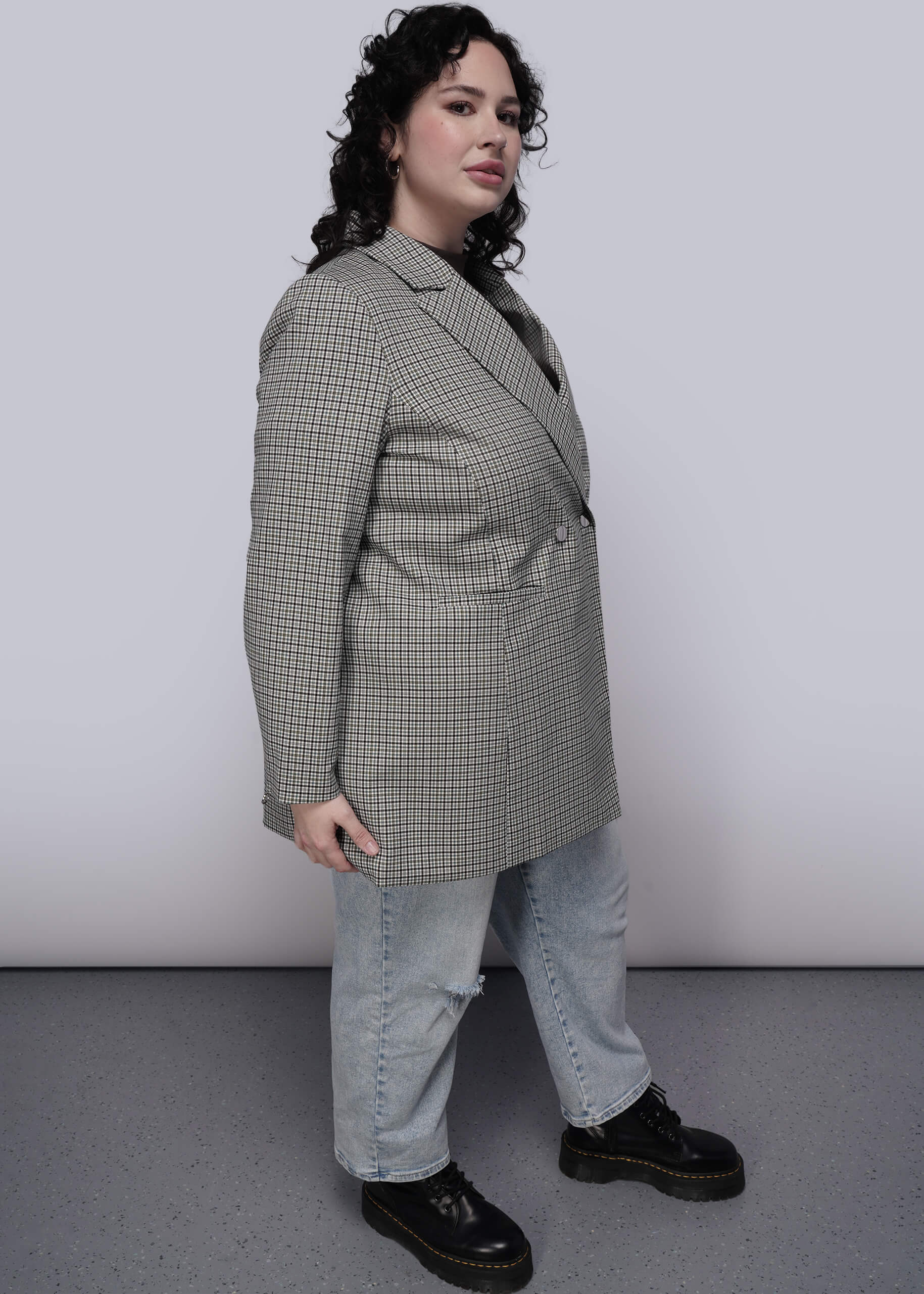 1X=Side view of person wearing a plaid blazer and jeans with a plain background
