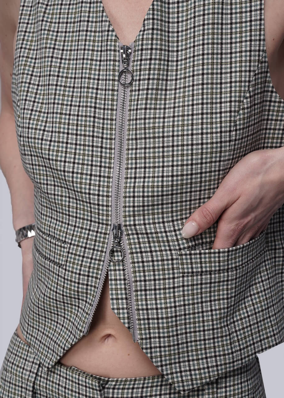S=Close up of checkered vest with a zipper detail on a plain background