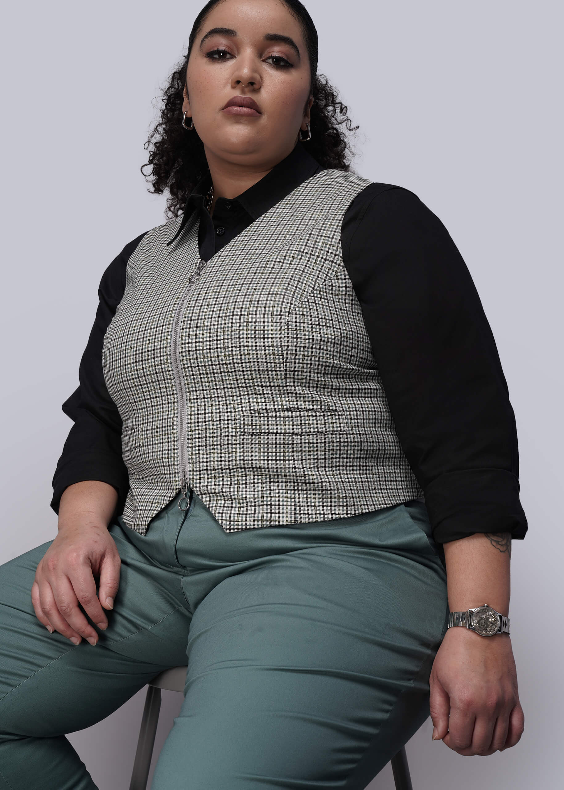 1X=Person wearing a checkered vest over a black shirt with green pants on a plain background