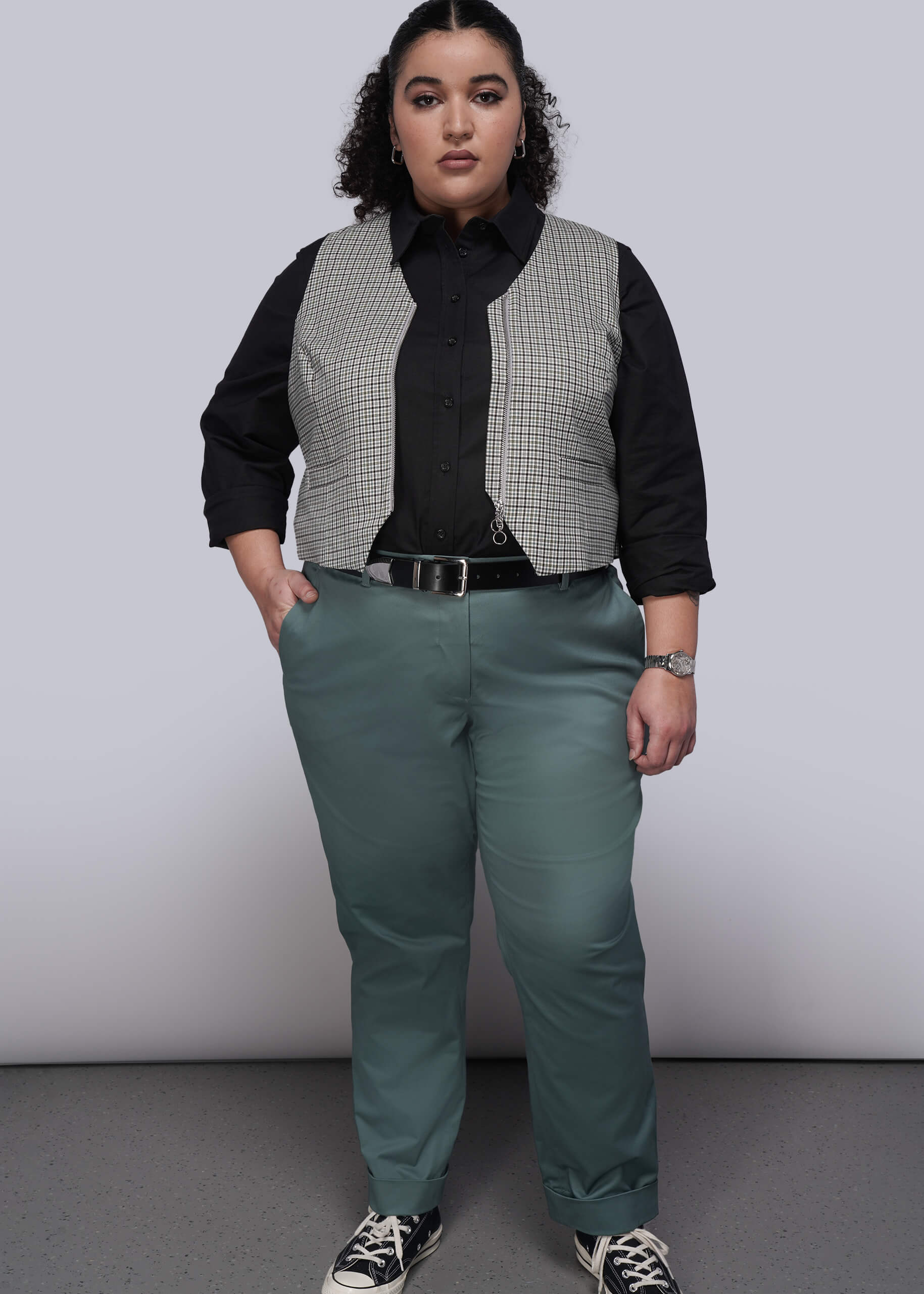 1X=Person wearing a black shirt, plaid vest, and green pants against a plain background