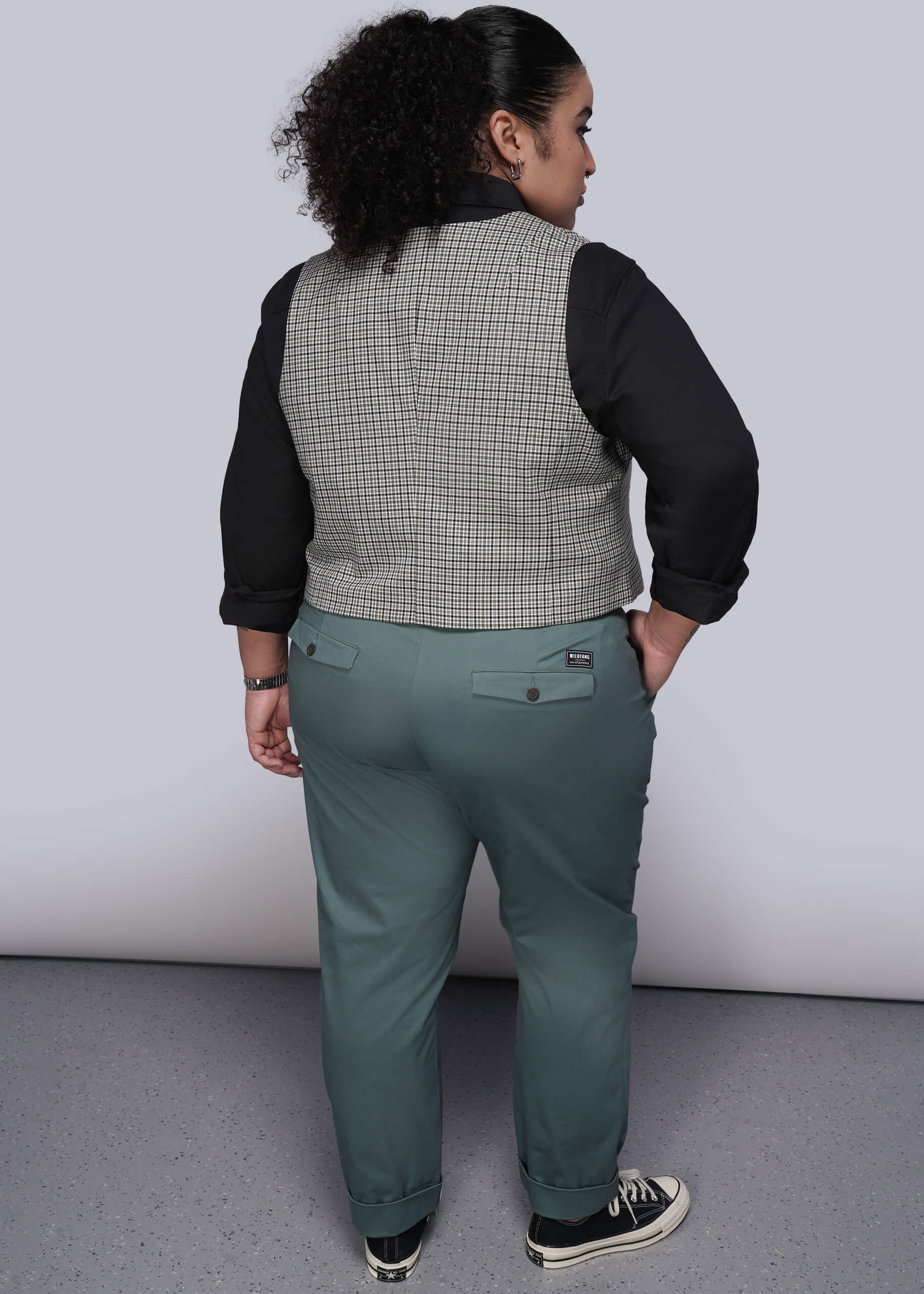 1X=Person wearing a checkered vest over a black long-sleeve shirt with green pants on a plain background