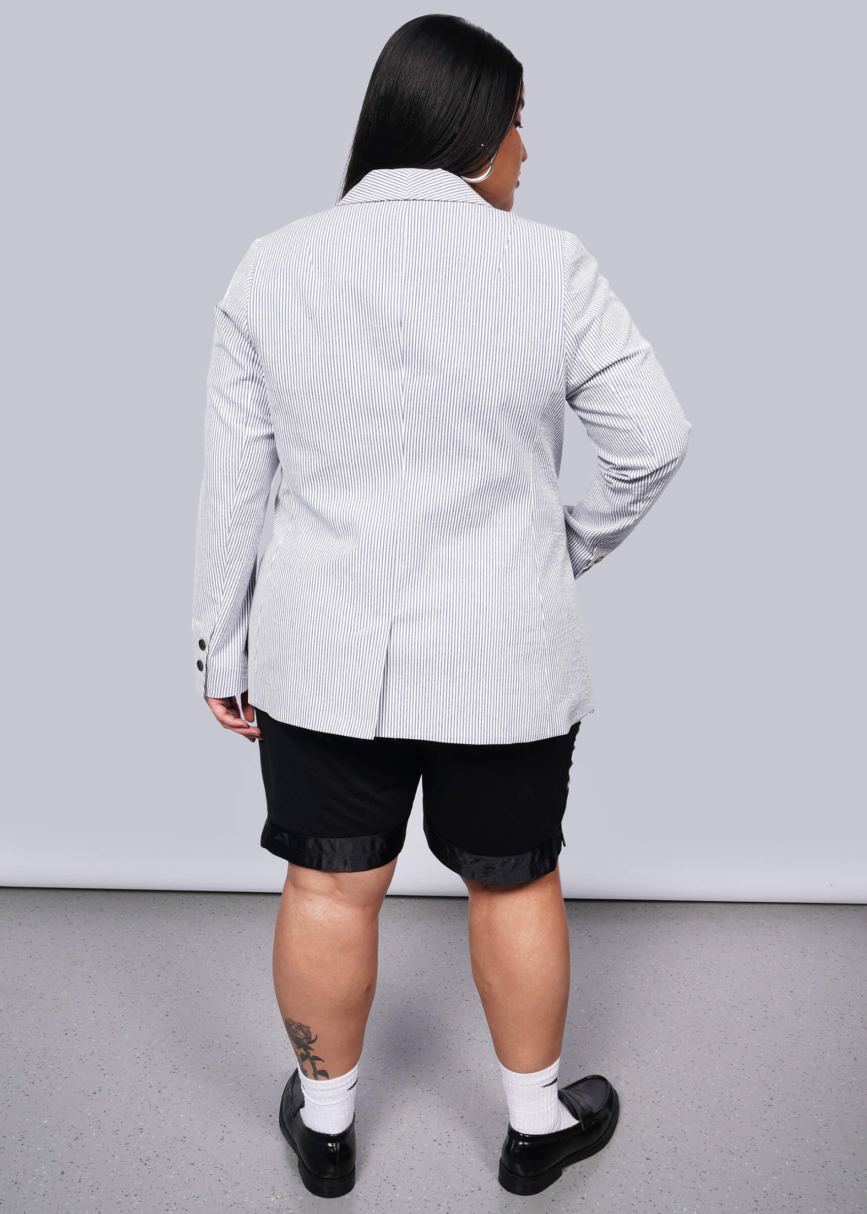 1X=Person wearing a light blue striped blazer over a black top with black shorts on a plain background