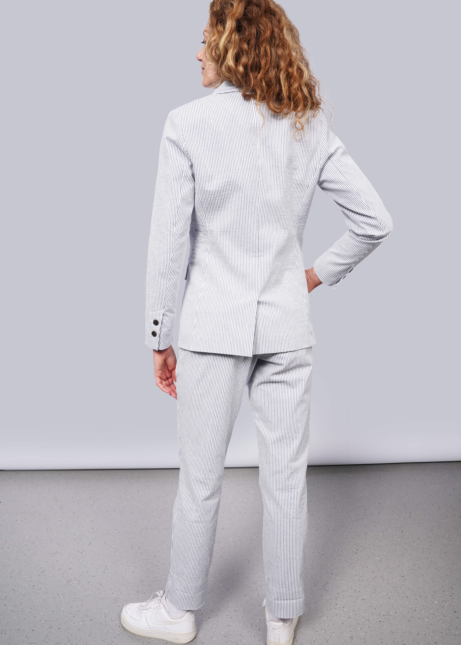 S=Person wearing a light blue suit standing against a plain background