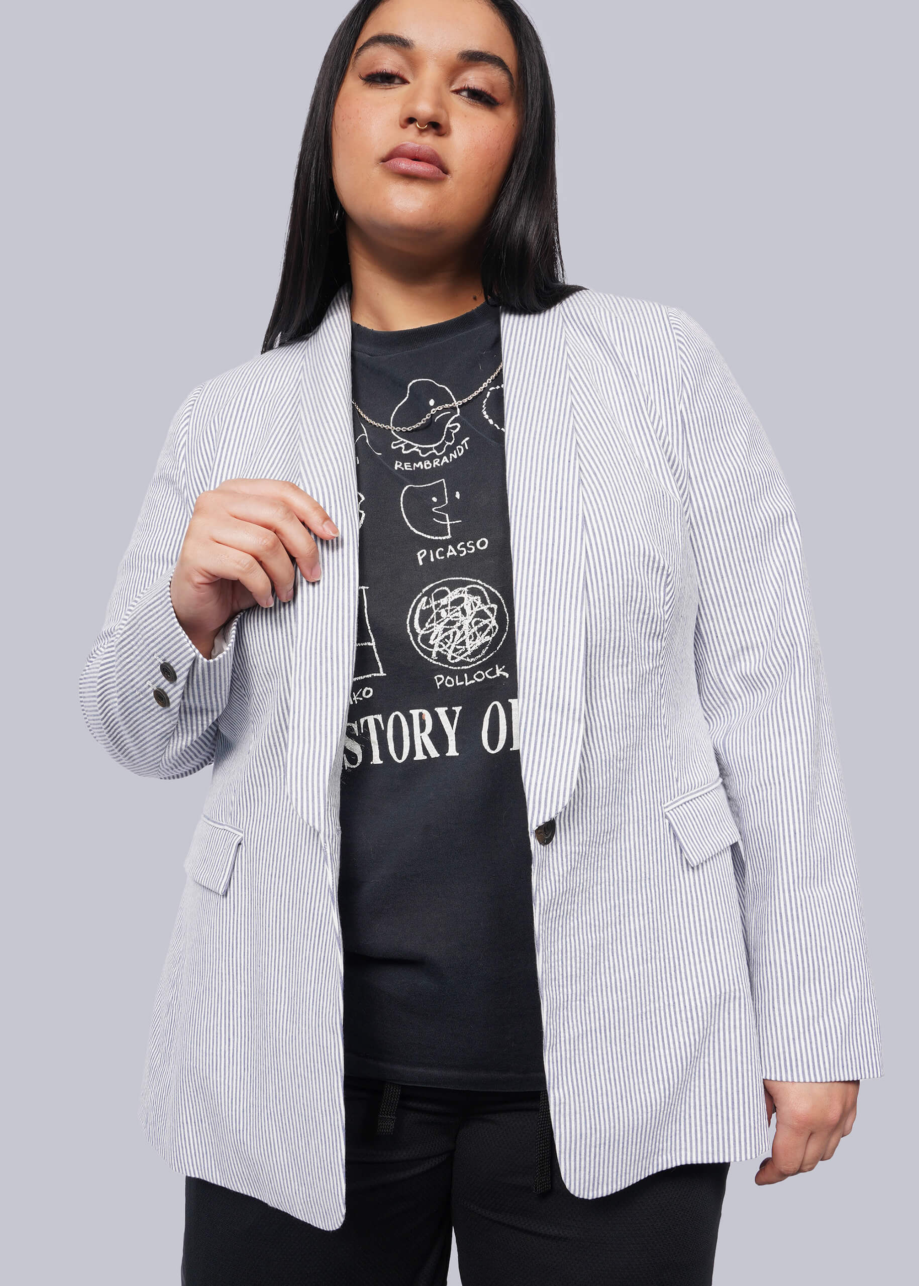 1X=Person wearing a light blue blazer over a black graphic t-shirt on a plain background