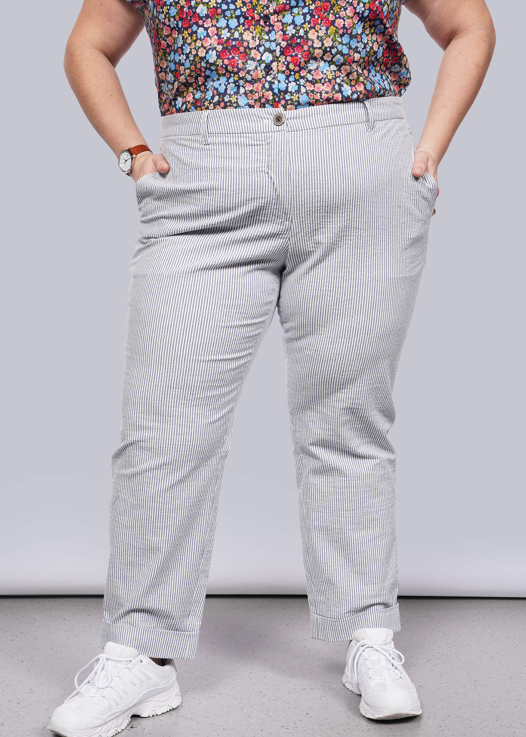 1X=Person wearing light blue seersucker pants with a colorful floral top on a plain background