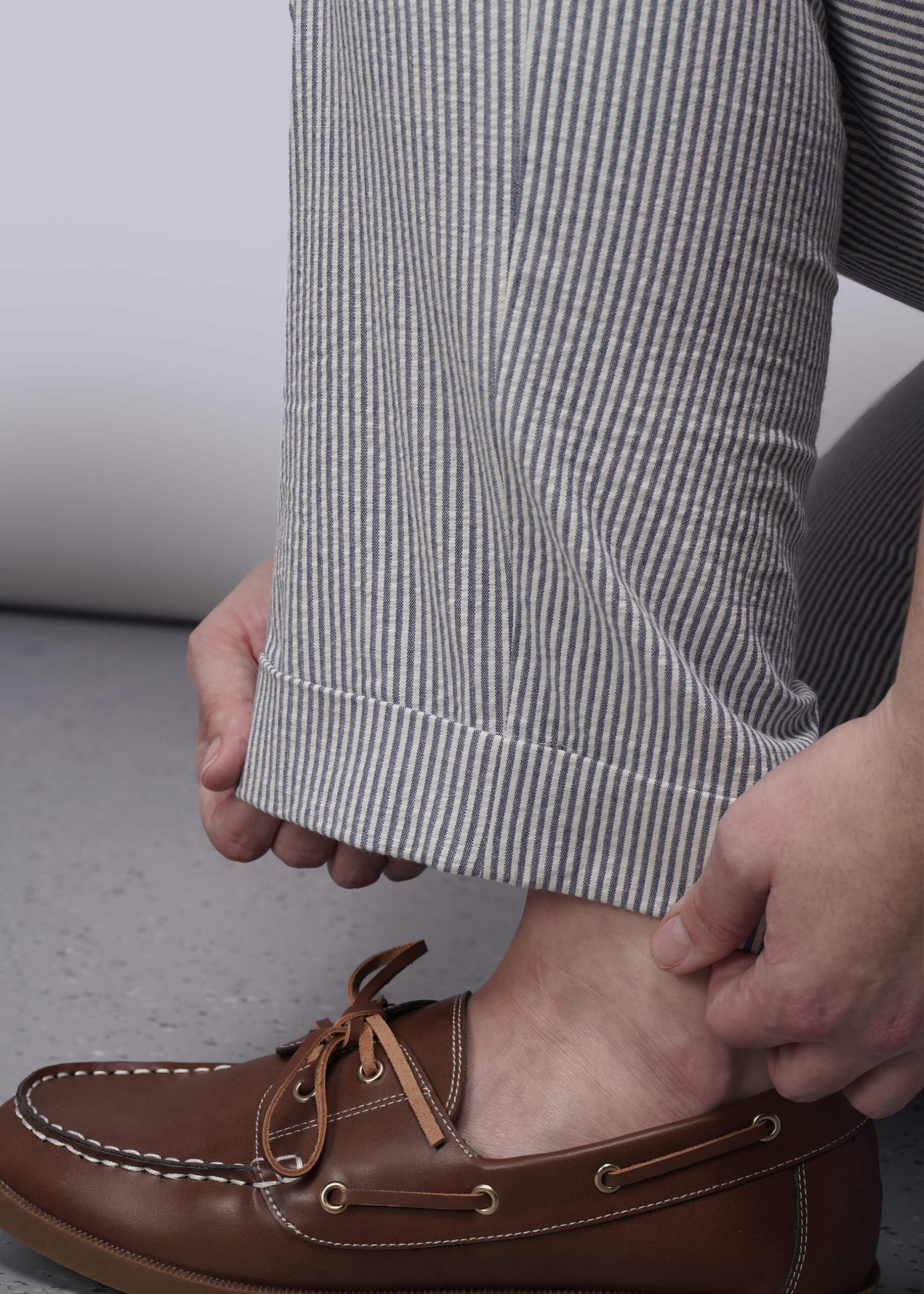 S=Brown leather boat shoes with white laces worn with striped pants on a neutral background