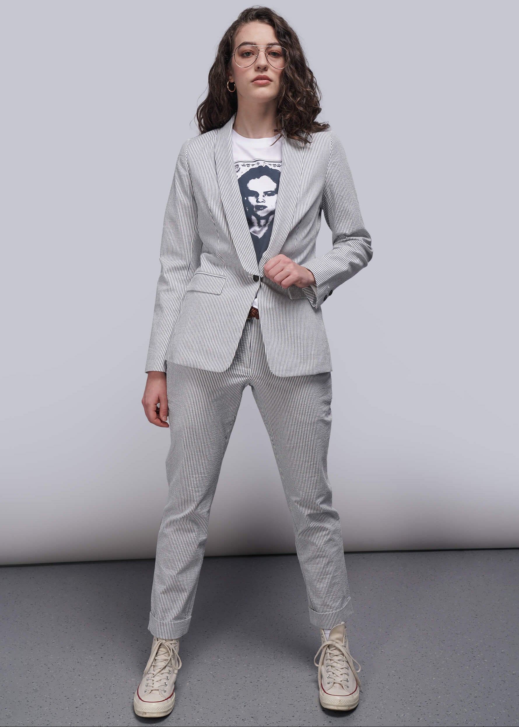 S=Person wearing a light blue striped seersucker suit with a graphic t-shirt underneath on a plain background