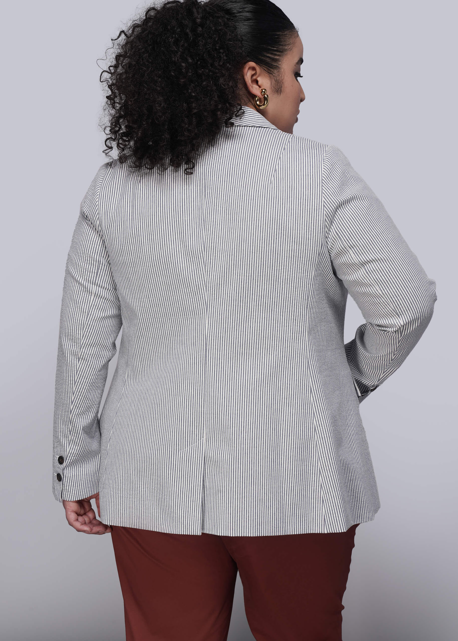 1X=Back of person wearing a light blue striped seersucker blazer and red pants on a white background