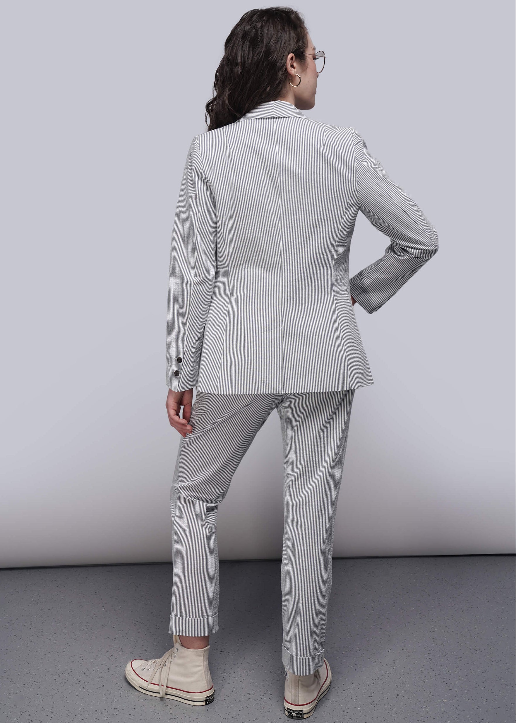 S=Back of person wearing a light blue striped seersucker suit standing against a plain background