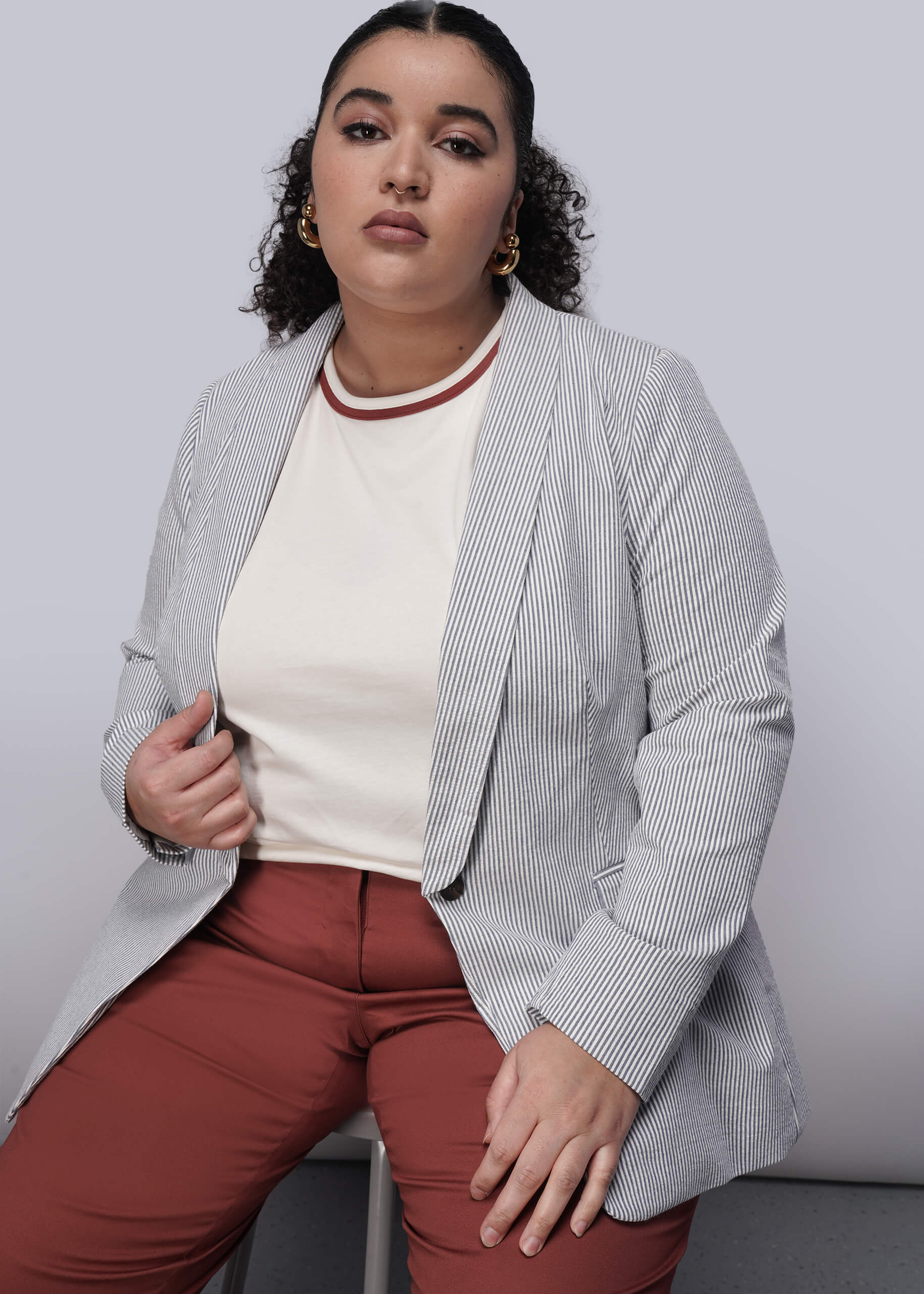 1X=Person wearing a light blue striped seersucker blazer over a white shirt with a red pattern, paired with red pants, against a plain background.