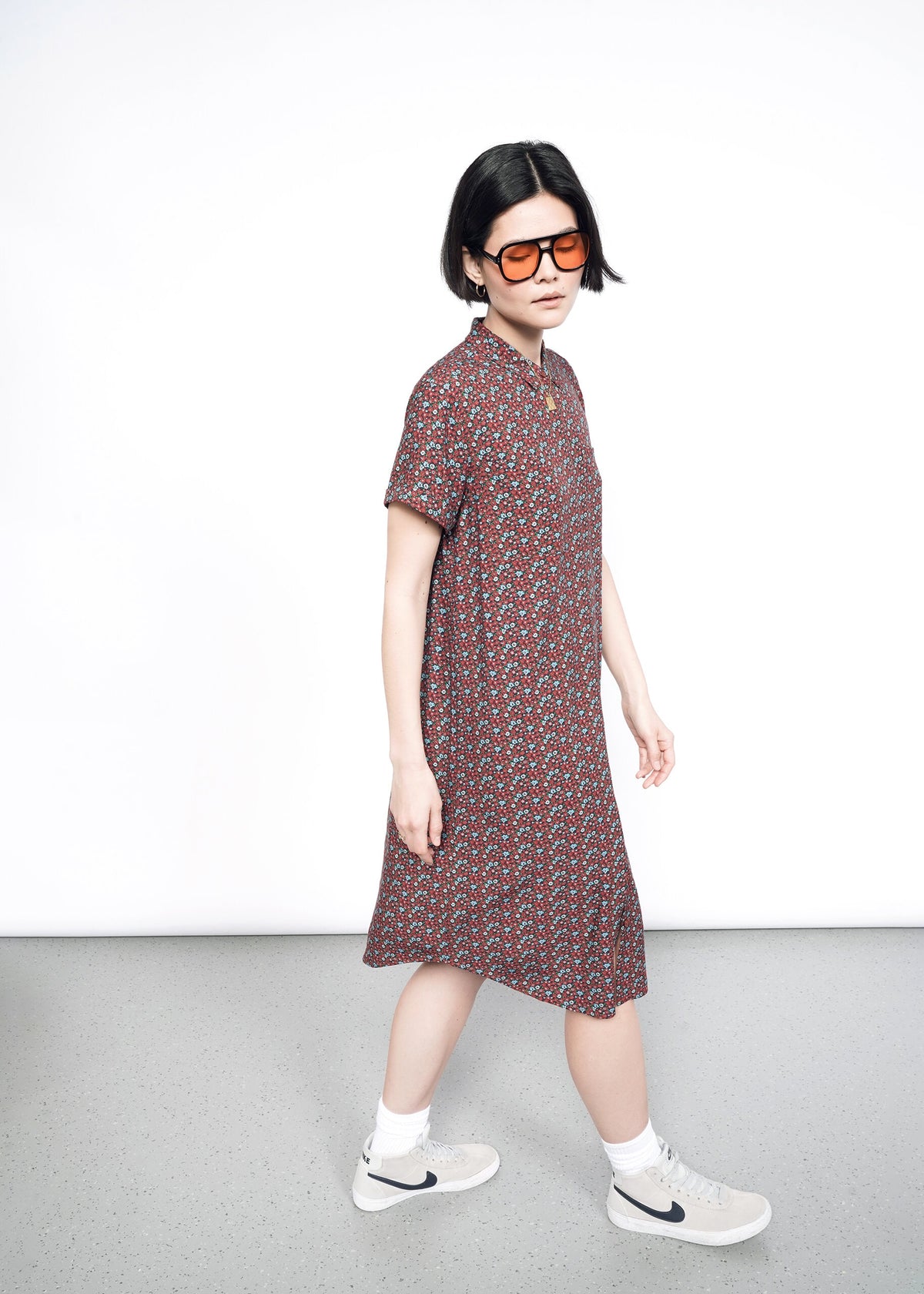 Side image of Model wearing the Empower Short Sleeve Shirt Dress in Floral Cinnamon in size S, with sunglasses, white socks, and tan sneakers