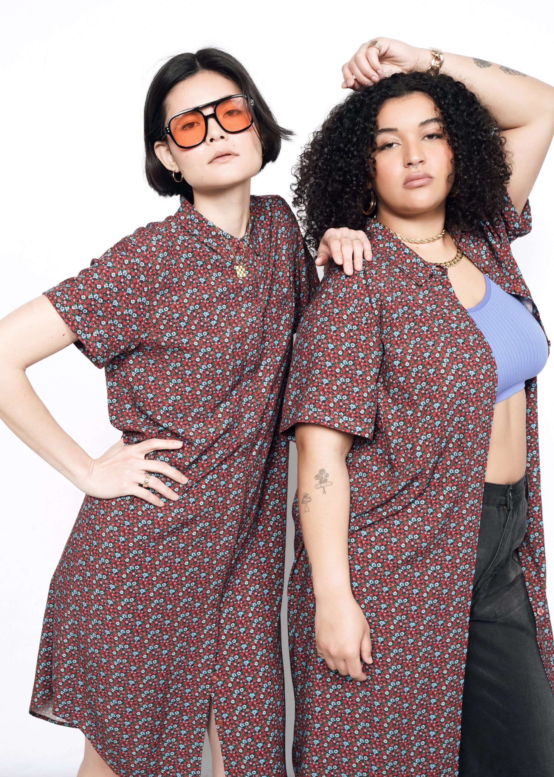 2 Models wearing the Empower Short Sleeve Shirt Dress in Floral Cinnamon. One in size S, with sunglasses. One in size 1X with a purple bra and black pants.