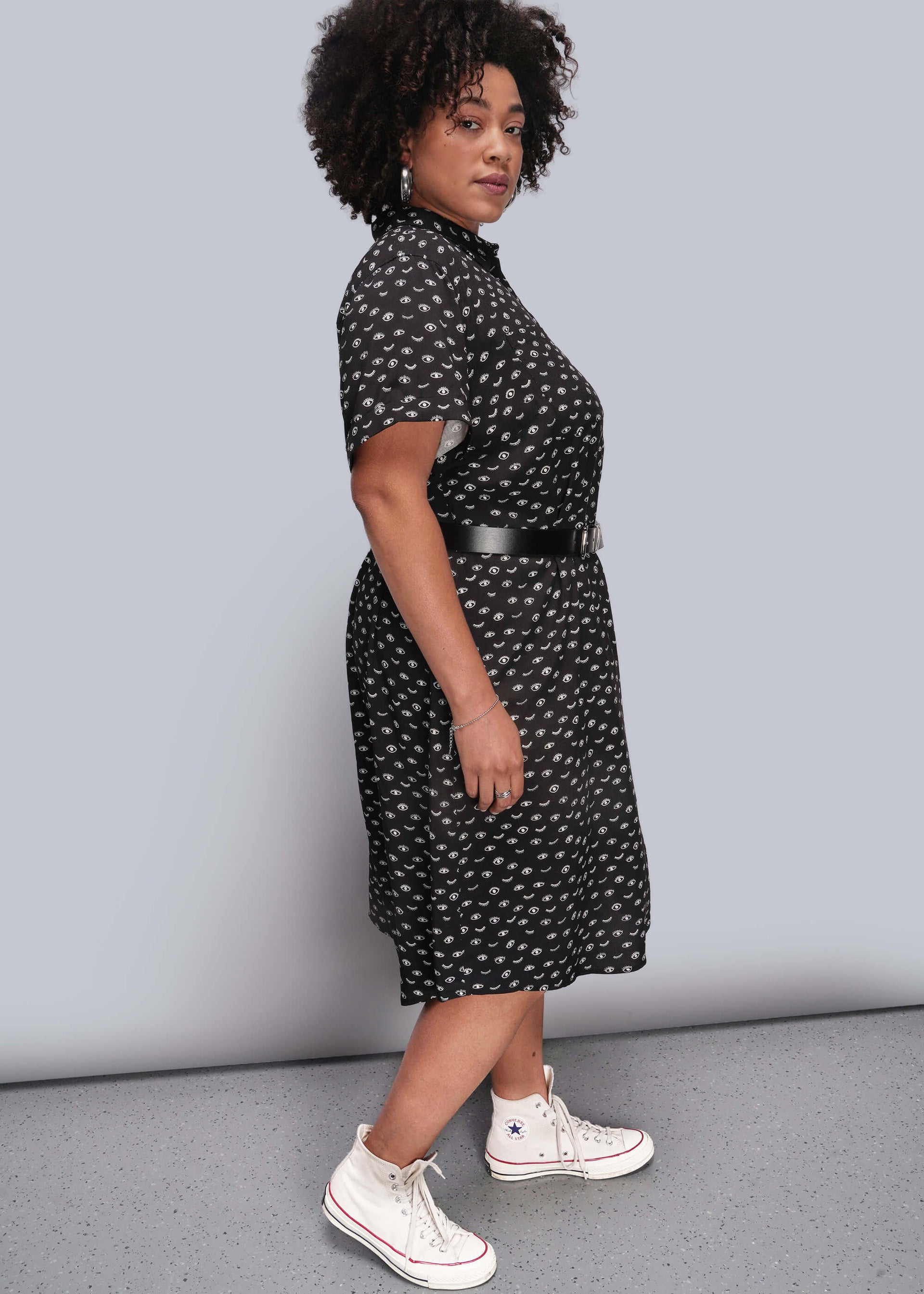 1X=Person wearing a black patterned dress with white sneakers on a plain background