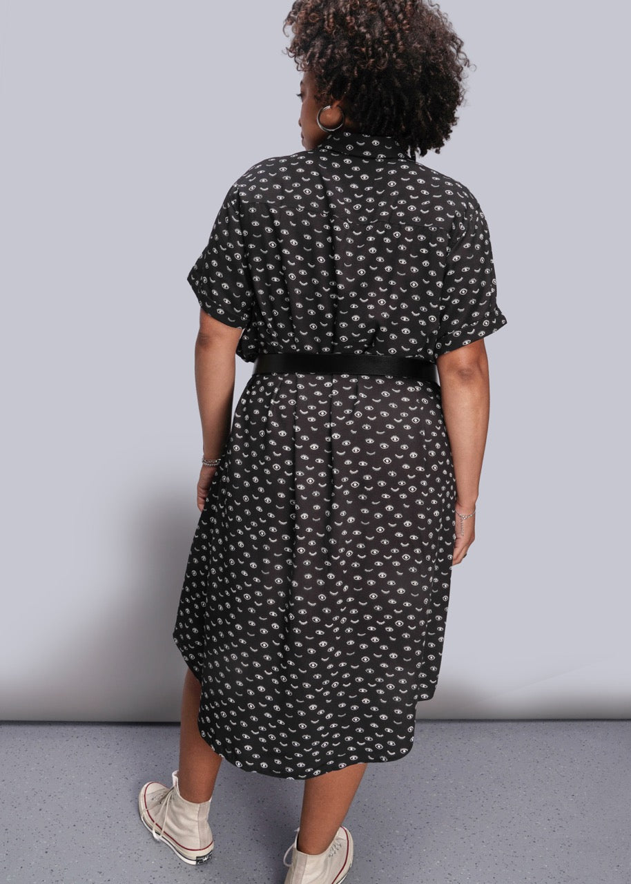 1X=Person wearing a black patterned dress against a plain background