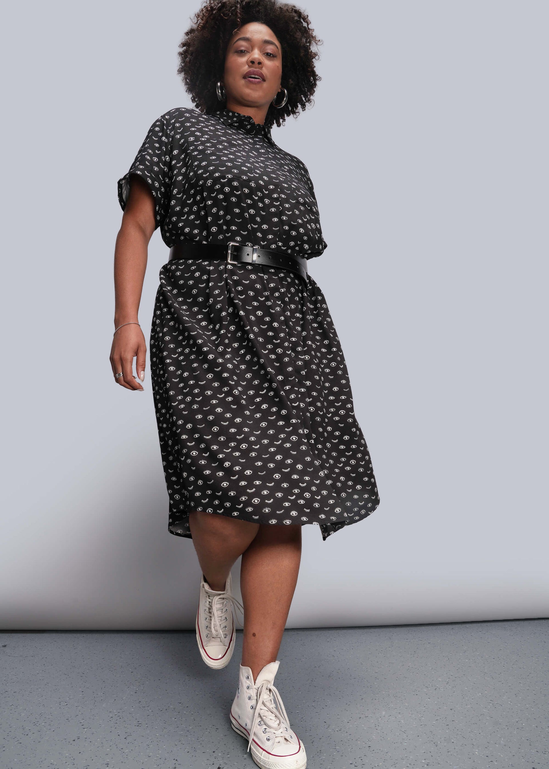 1X=Person wearing a black patterned dress with white sneakers on a plain background