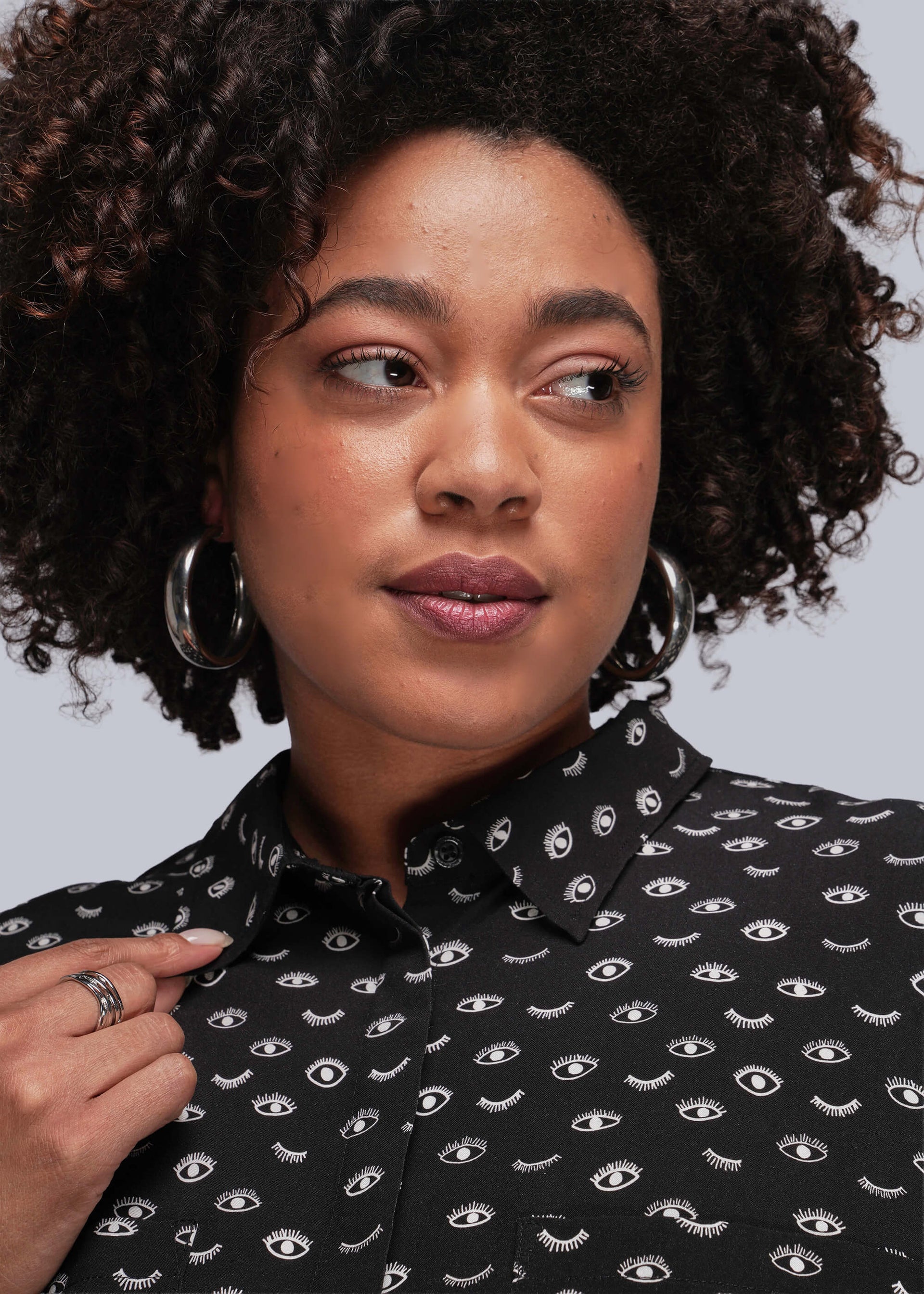 1X=Person wearing a black dress with eye pattern against a gray background