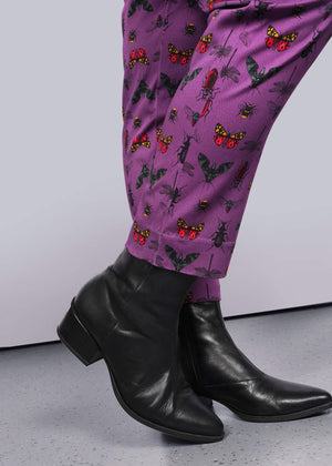S=Close up view of bottom hems of purple bug printed pant. Also visible are model's black heeled boots.