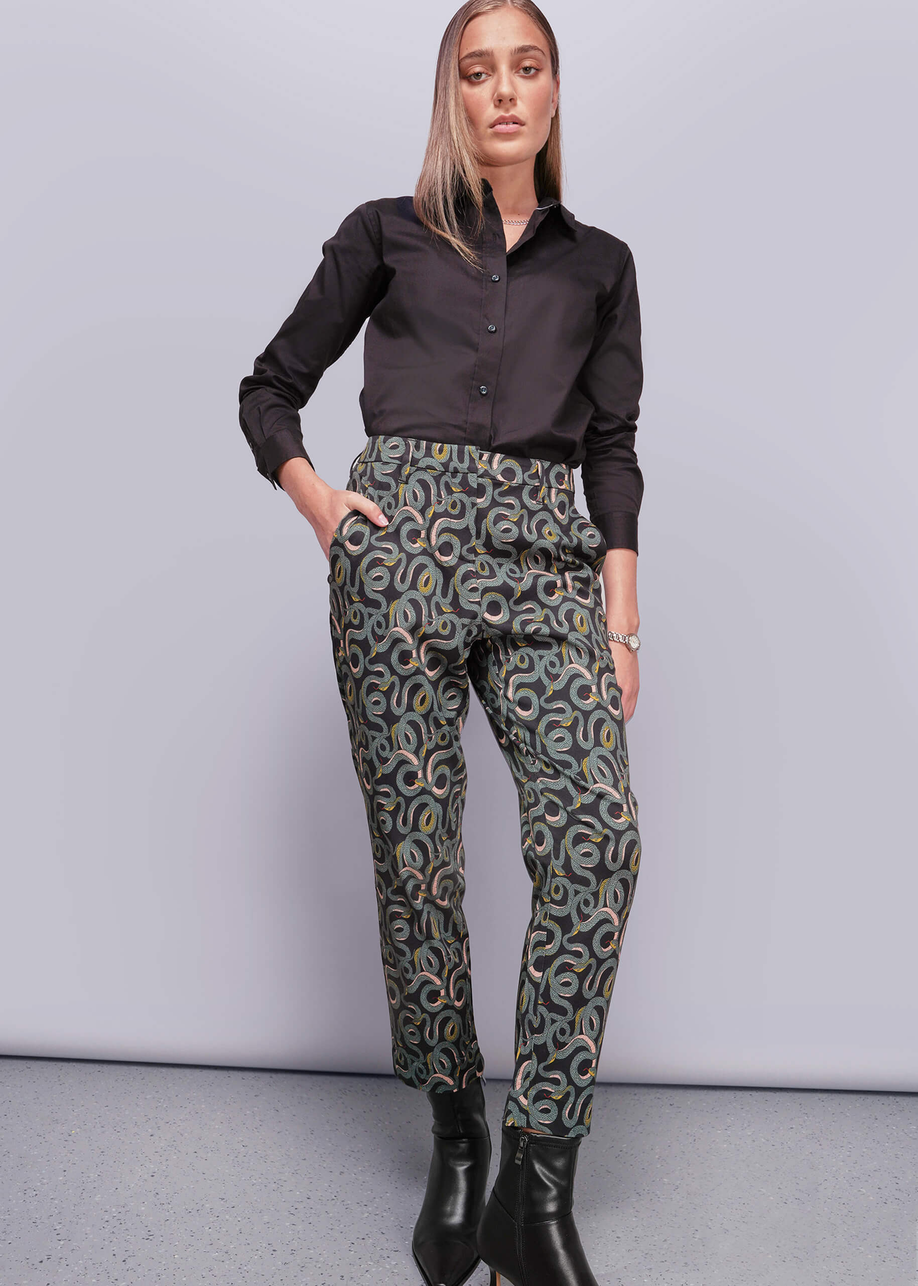 S=Woman wearing a black shirt and patterned pants against a gray background