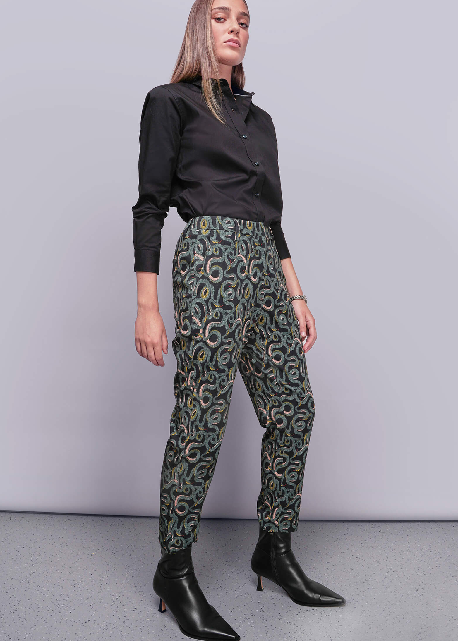 S=Woman wearing a black shirt and patterned pants against a plain background