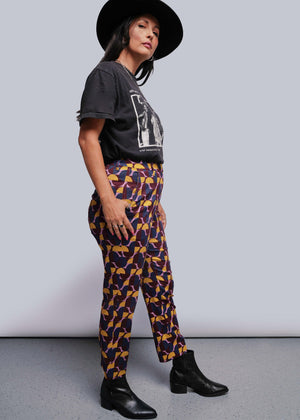 S=Woman wearing a black t-shirt and patterned pants against a gray background