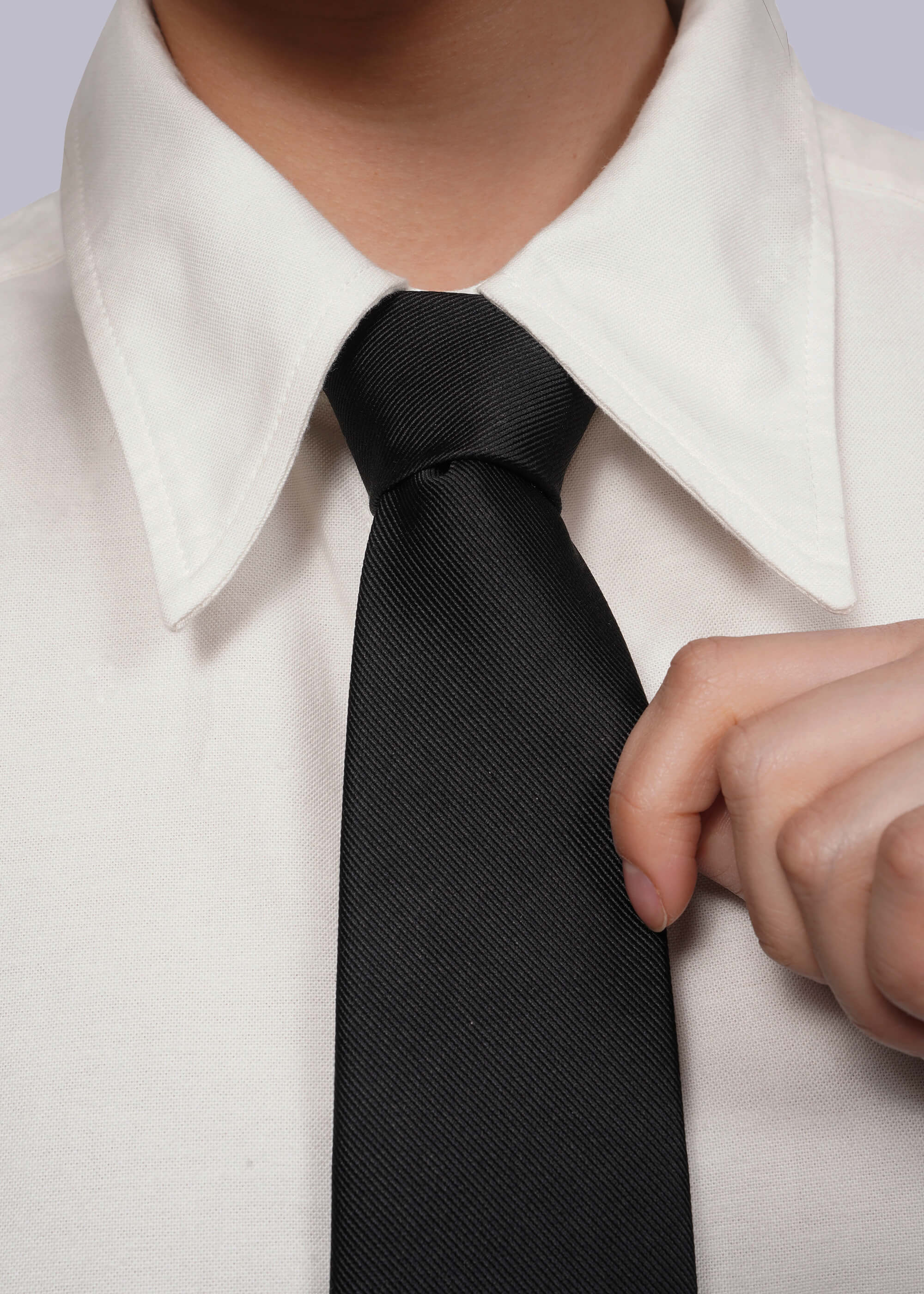 Close up of black tie on white shirt with model's hand holding tie.