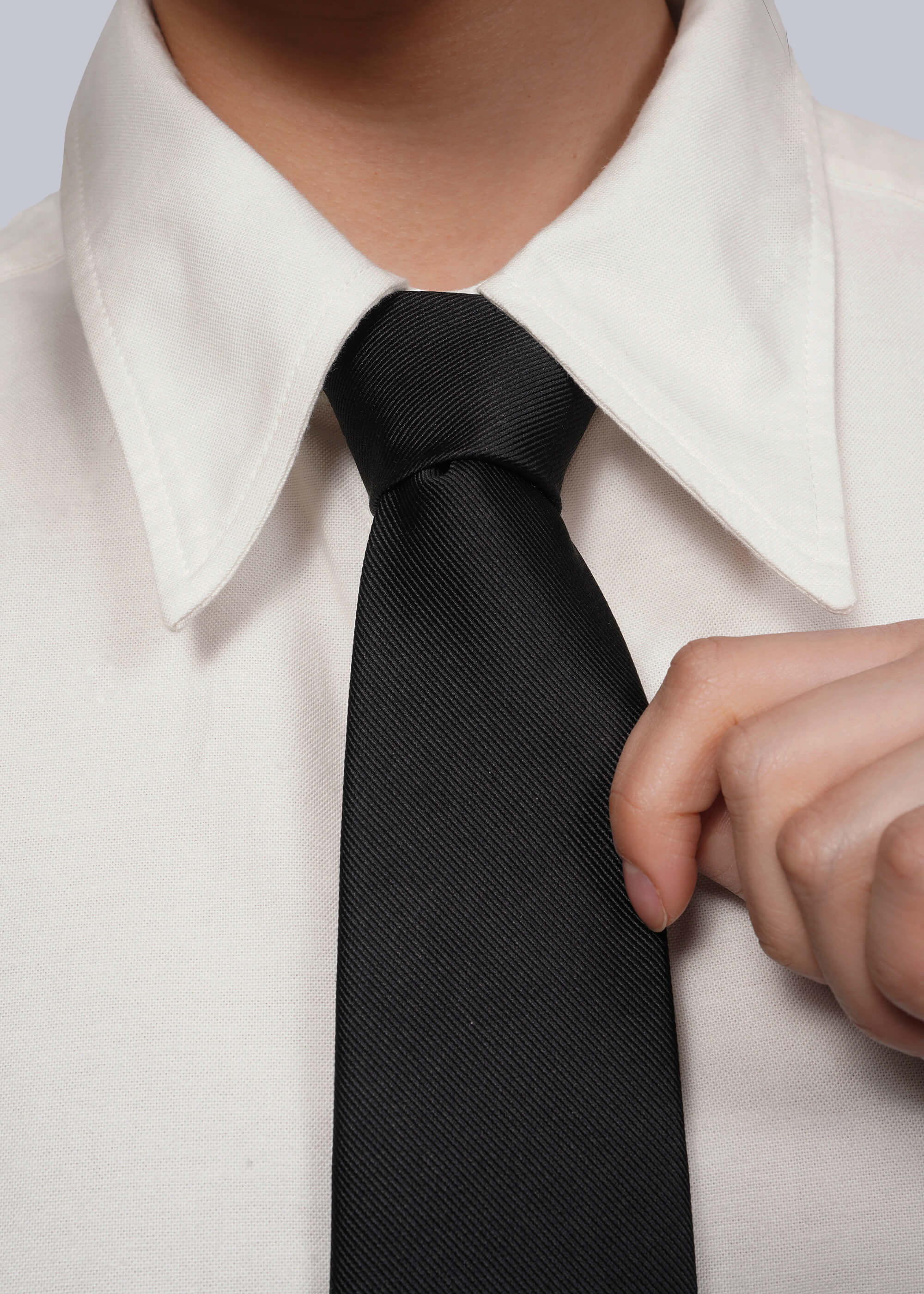 Close up of black tie on white shirt with model's hand holding tie.
