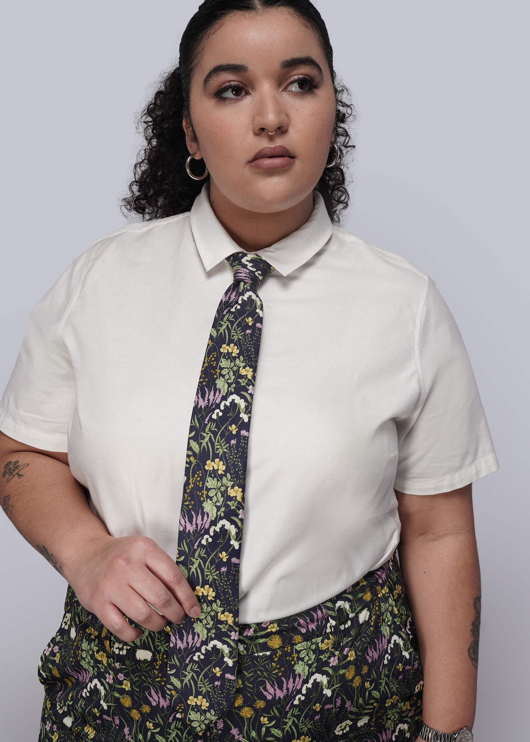 Person wearing a white shirt with a floral tie and dark floral pants against a plain background