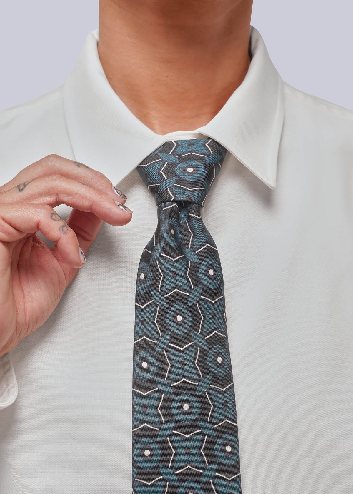 A close-up of a person wearing a white collared dress shirt and a patterned necktie in muted blue, gray, and white. A hand is adjusting the collar.