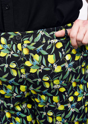 1X=Close up view of model with hand in front pant belt loop of The Empower Trouser in Citrus Black, which is a yellow and green print on black background featuring lemons and leaves. 