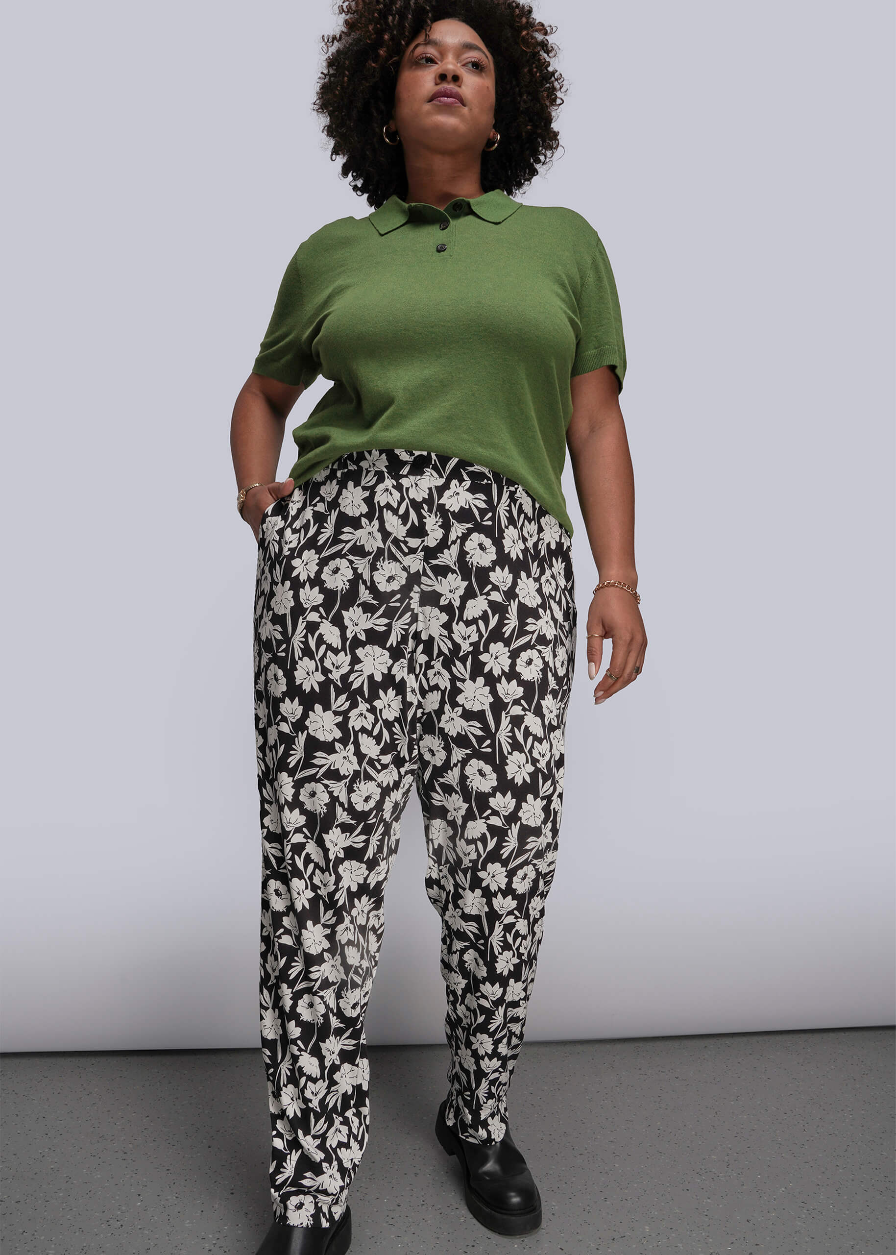 1X=Person wearing a green polo shirt and black and white floral pants against a plain background