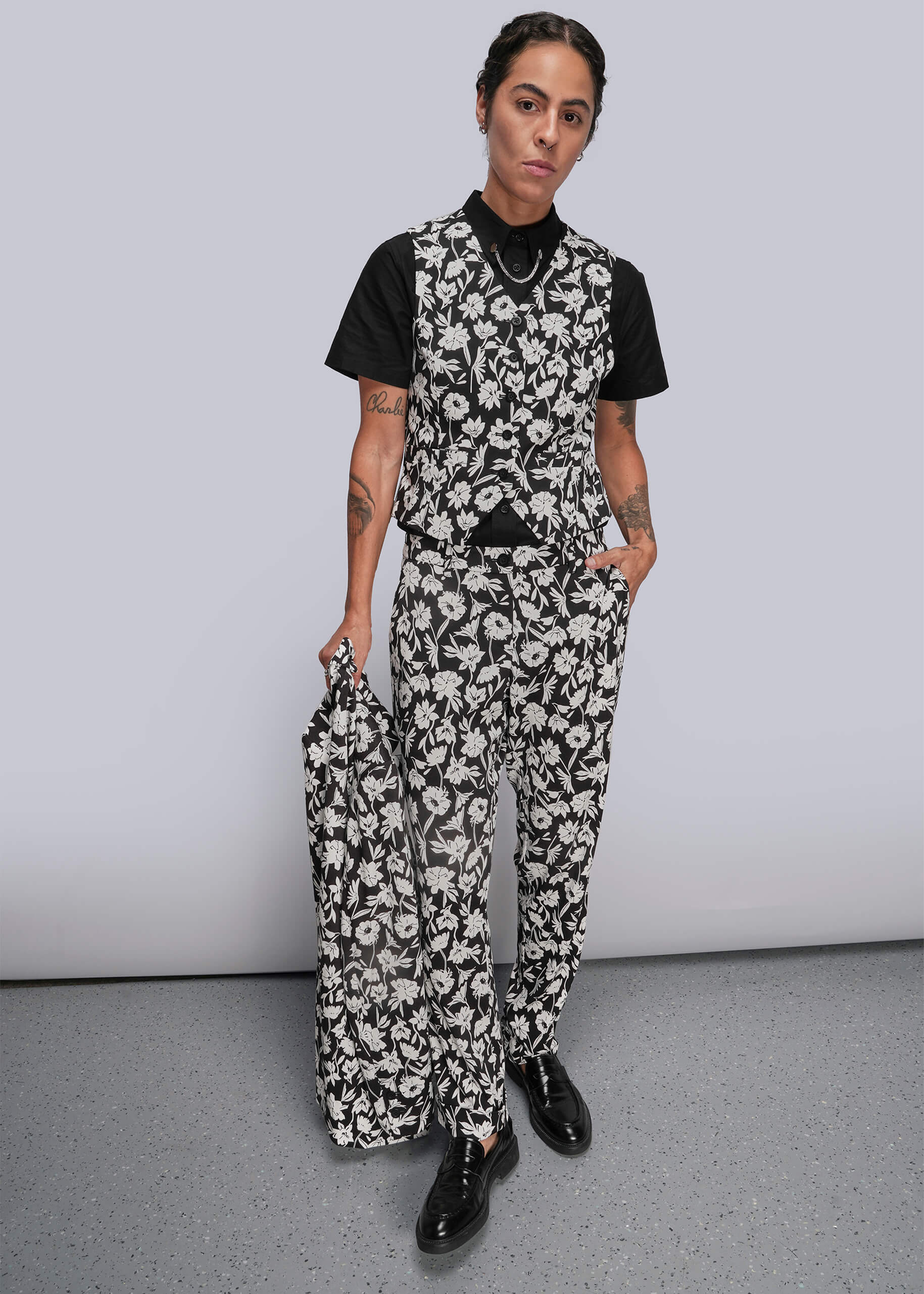 S=Person wearing a black and white floral suit with a plain background