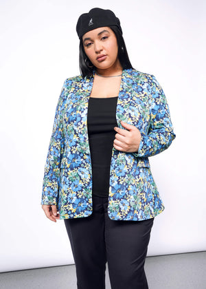 1X=Person with long black hair looks at camera wearing Kangol hat, black pants, and open floral patterned blazer with hand holding lapel.