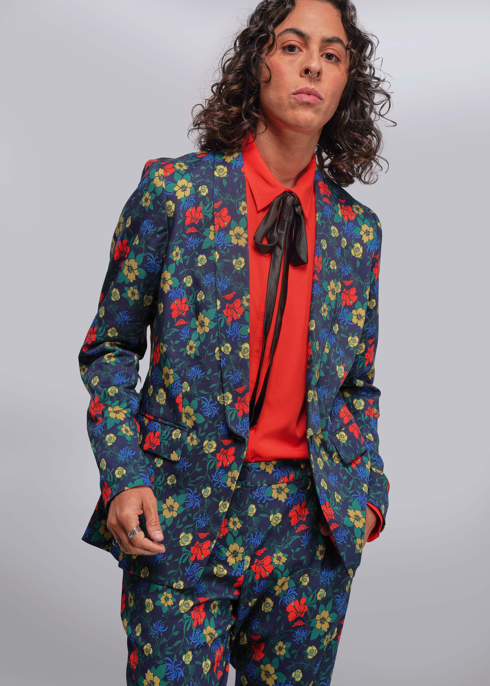 Person wearing a colorful floral suit with a red shirt and black tie against a gray background