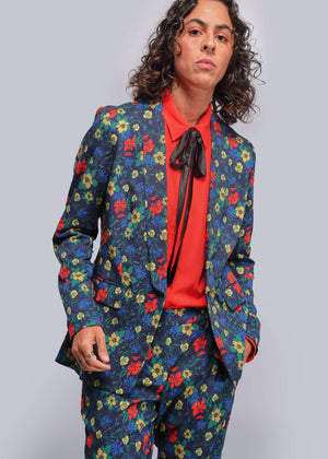 S=Person wearing a colorful floral suit with a red shirt and black tie against a gray background
