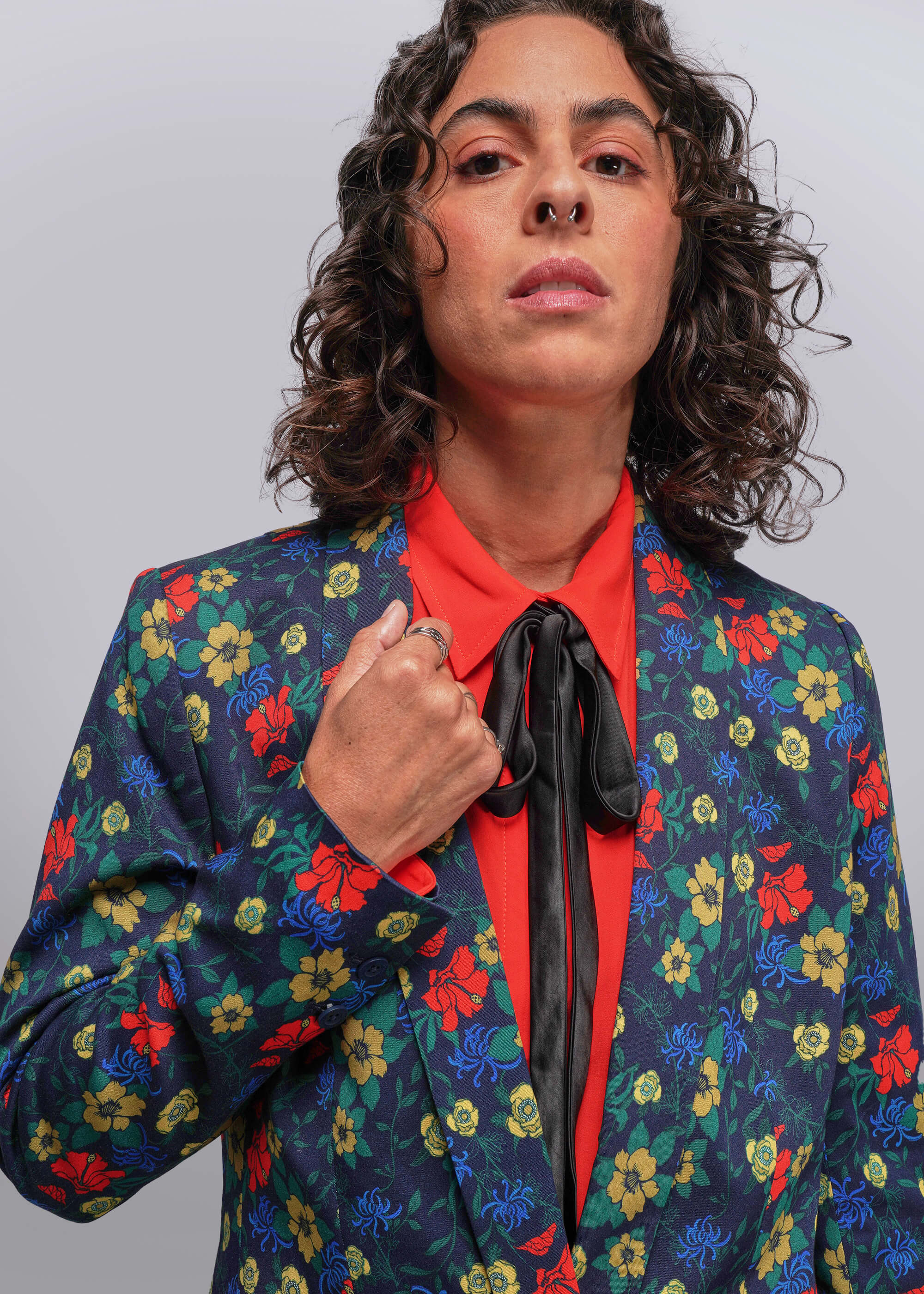 Person wearing a colorful floral blazer over a red shirt with a plain background