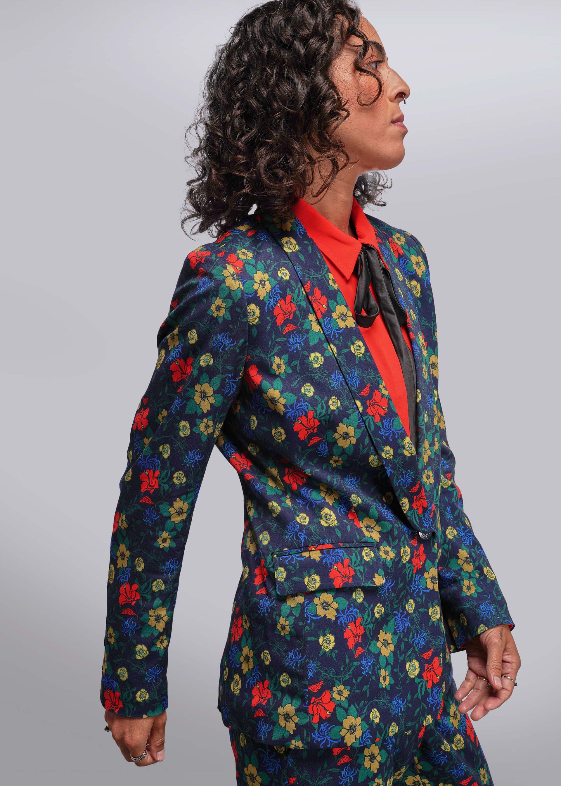 S=Person wearing a colorful floral suit with a red shirt on a gray background