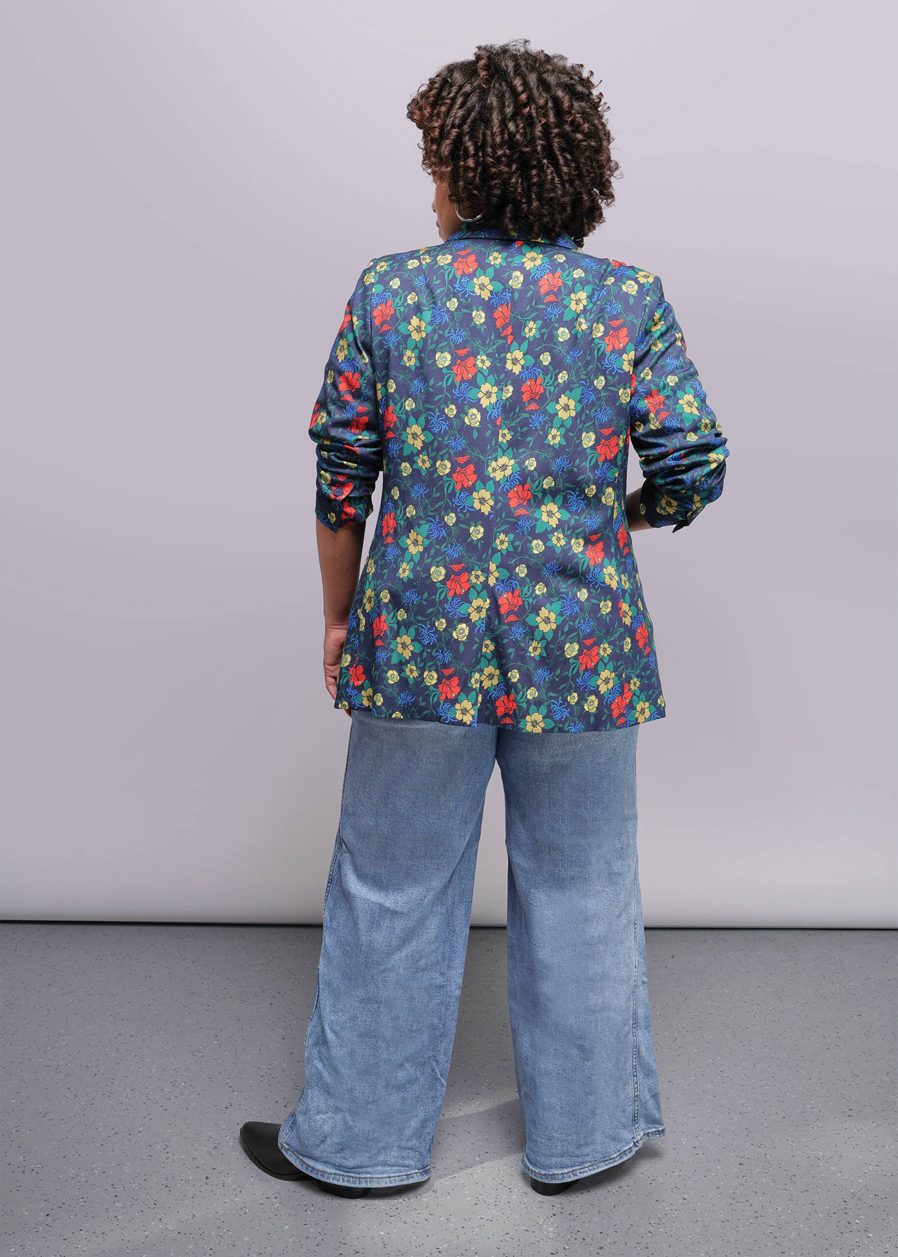 1X=Person wearing a colorful floral jacket and blue jeans against a plain background