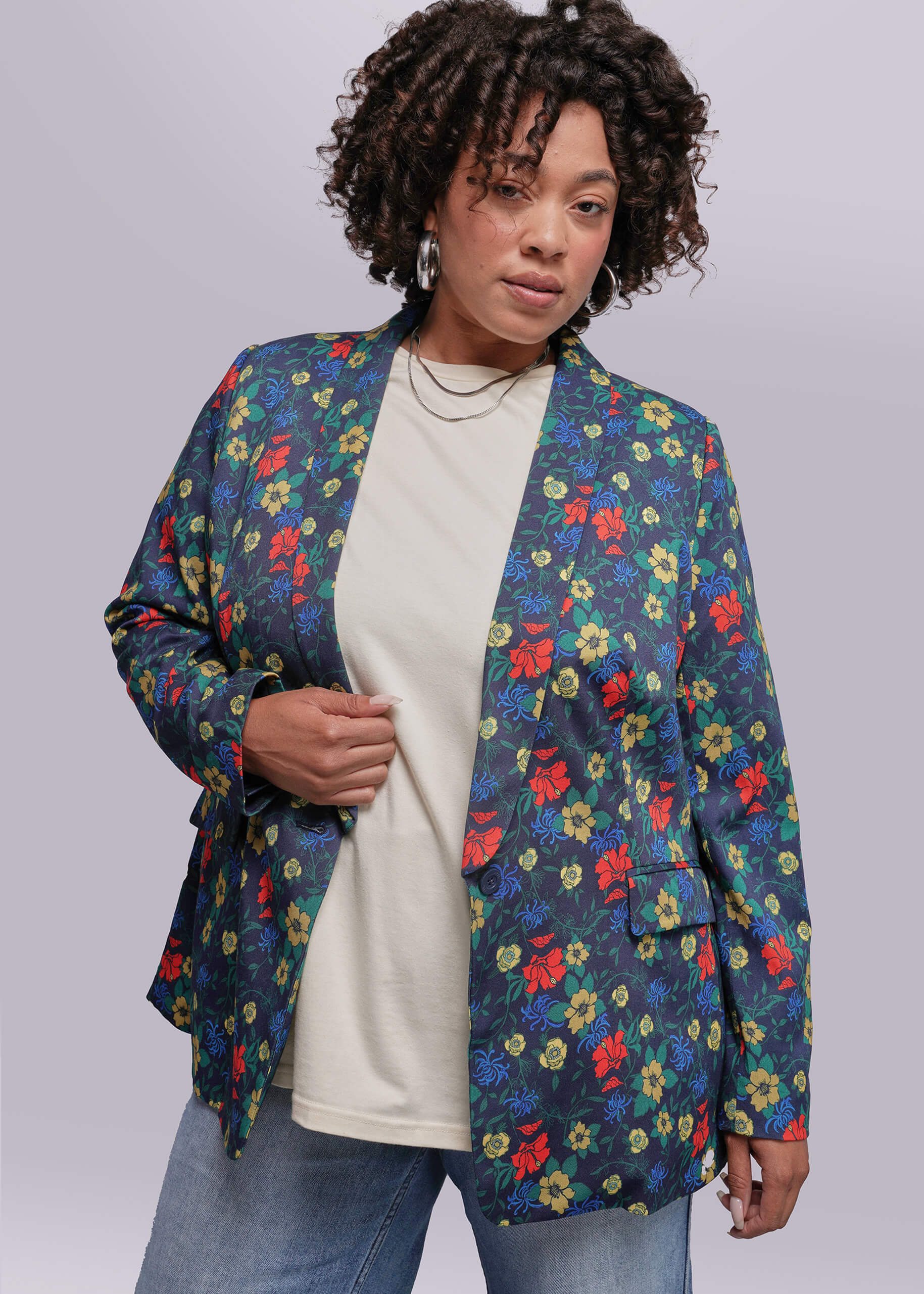 1X=Person wearing a colorful floral blazer over a white shirt and jeans on a plain background