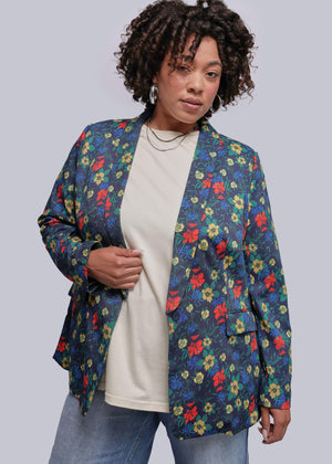 1X=Person wearing a colorful floral blazer over a white shirt and jeans on a plain background