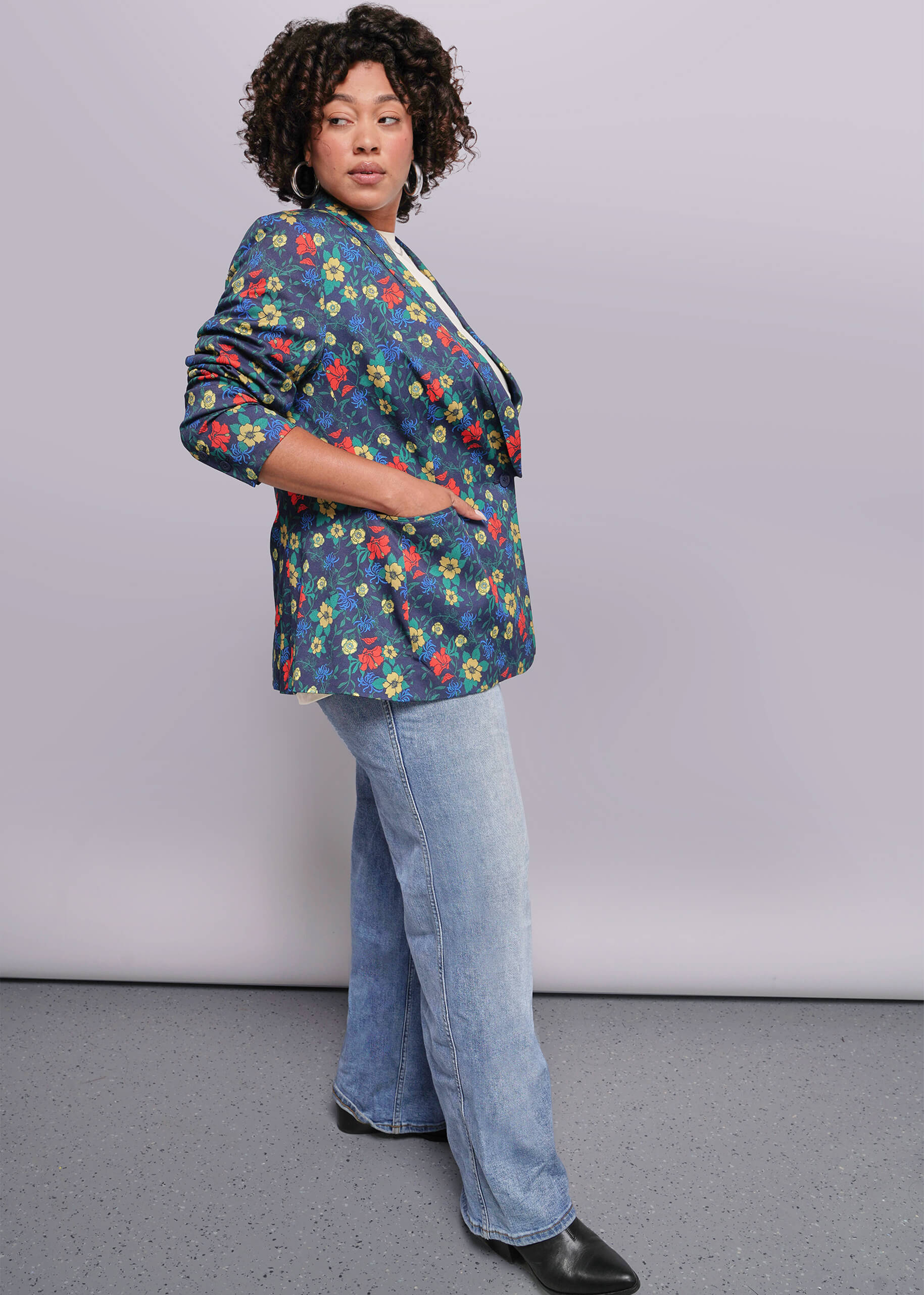 1X=Person wearing a colorful floral blazer and blue jeans against a plain background