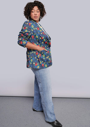 1X=Person wearing a colorful floral blazer and blue jeans against a plain background
