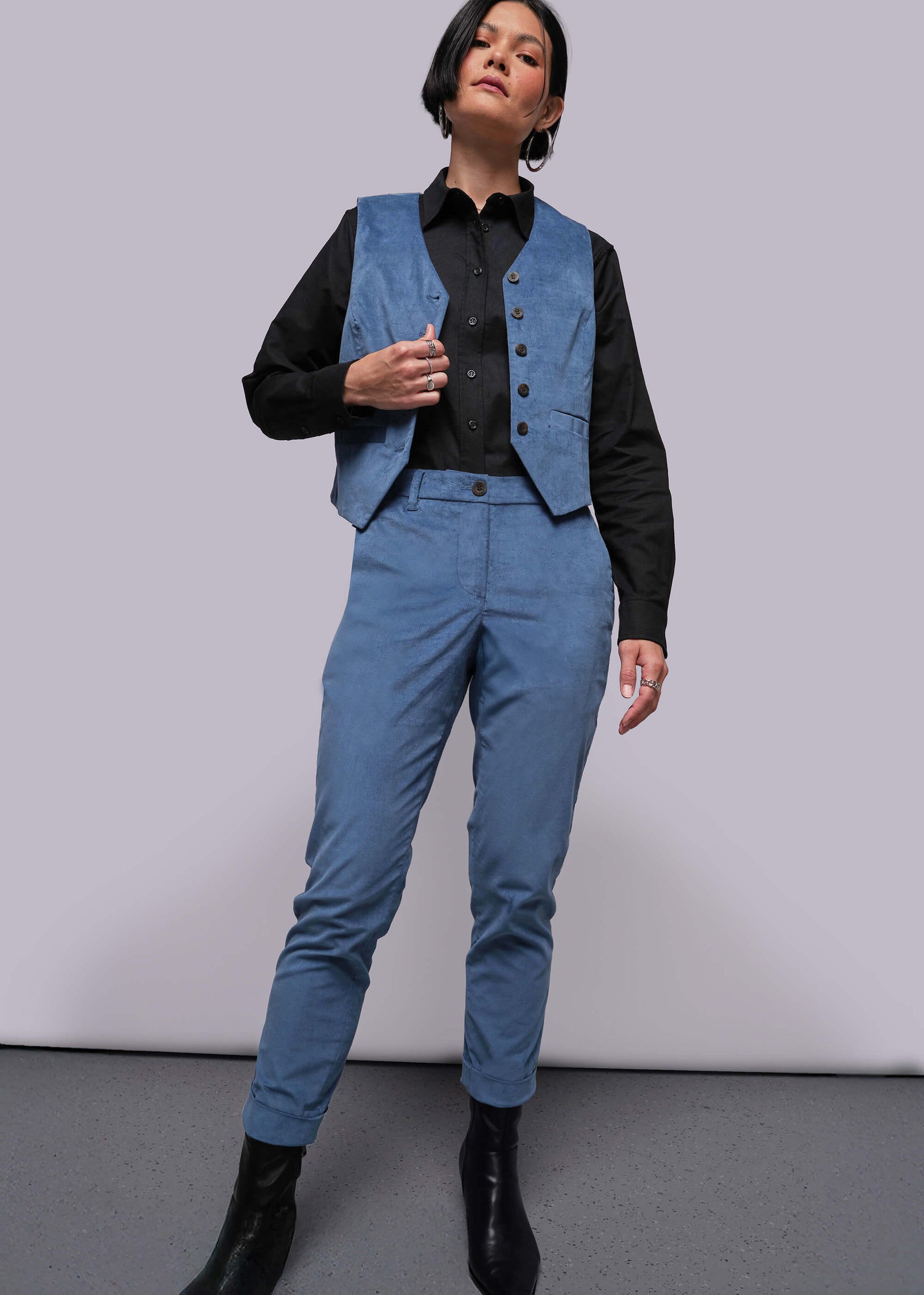 S=Person wearing a blue vest and pants with a black shirt against a plain background